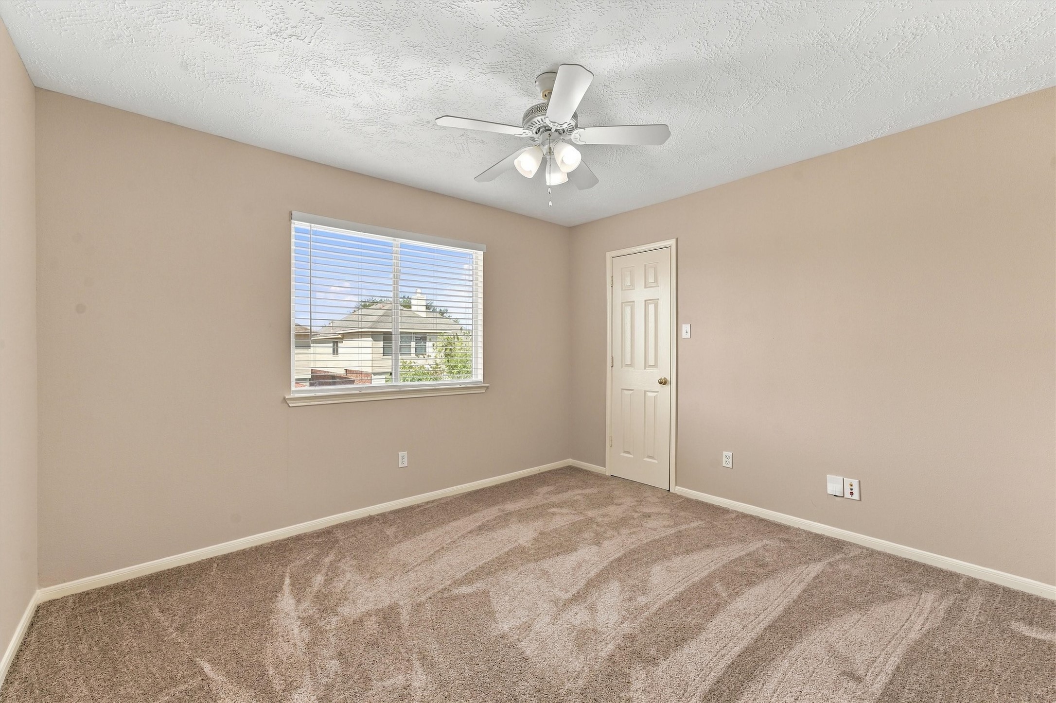 Cozy bedroom featuring neutral walls, a ceiling fan, and plush carpeting, with ample natural light streaming through the window.