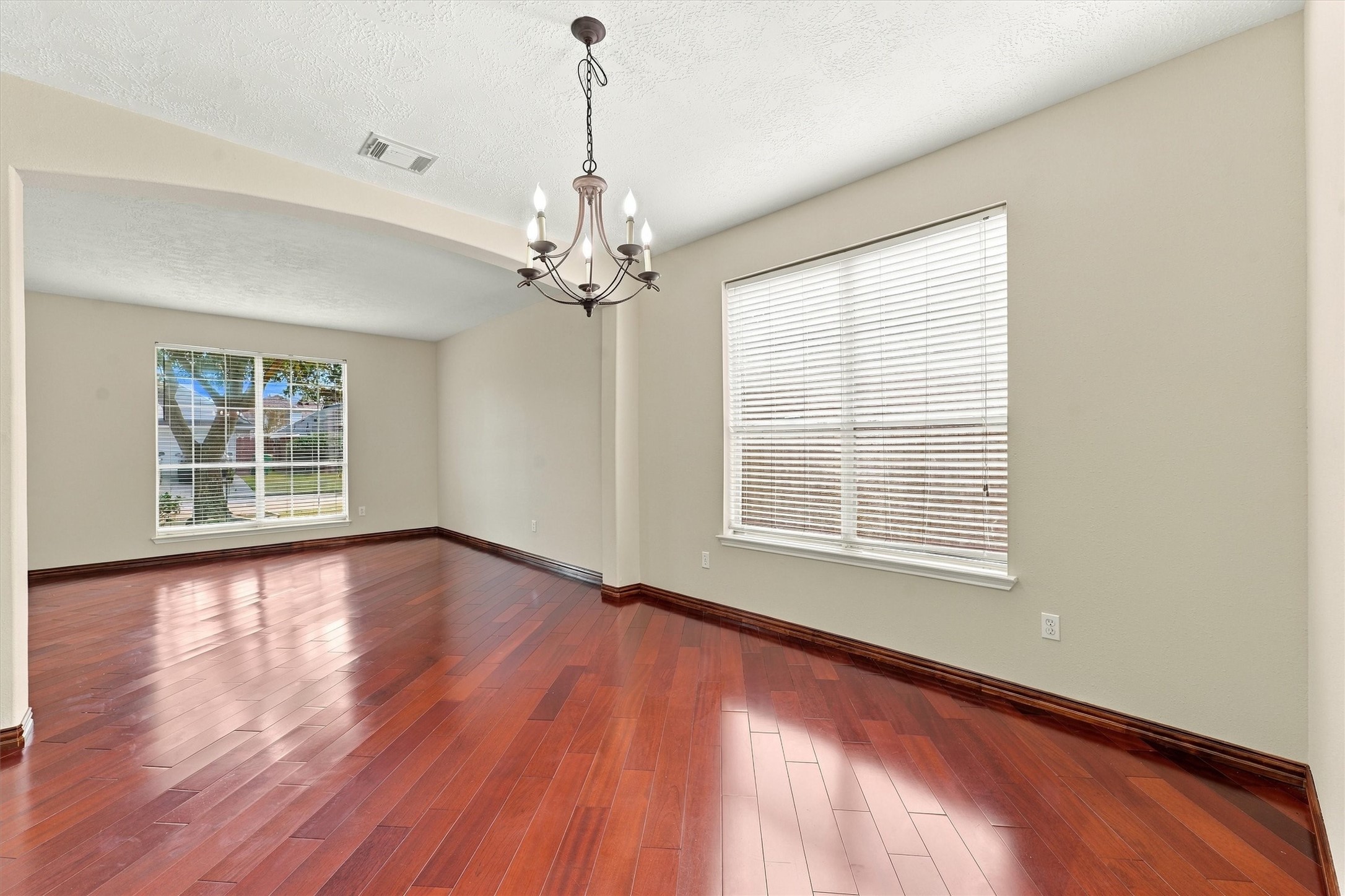 Elegant open living space featuring rich hardwood floors, abundant natural light from large windows, and a stylish chandelier for a touch of sophistication.