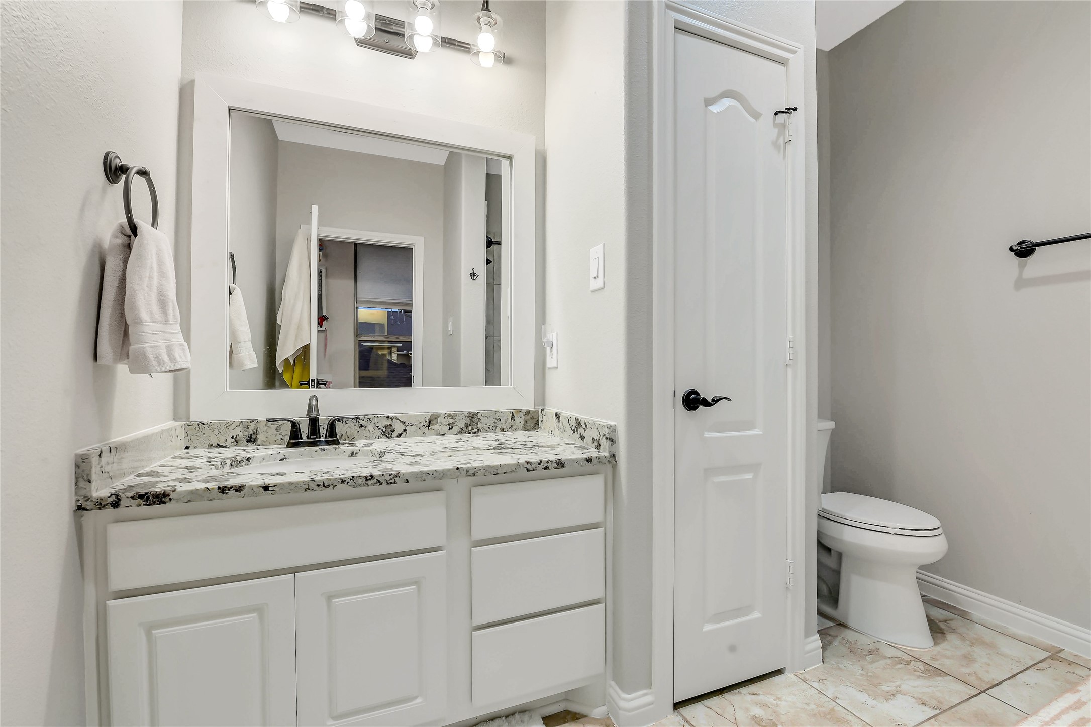 Bright ensuite bathroom with a granite vanity, tile floors, and convenient linen storage.