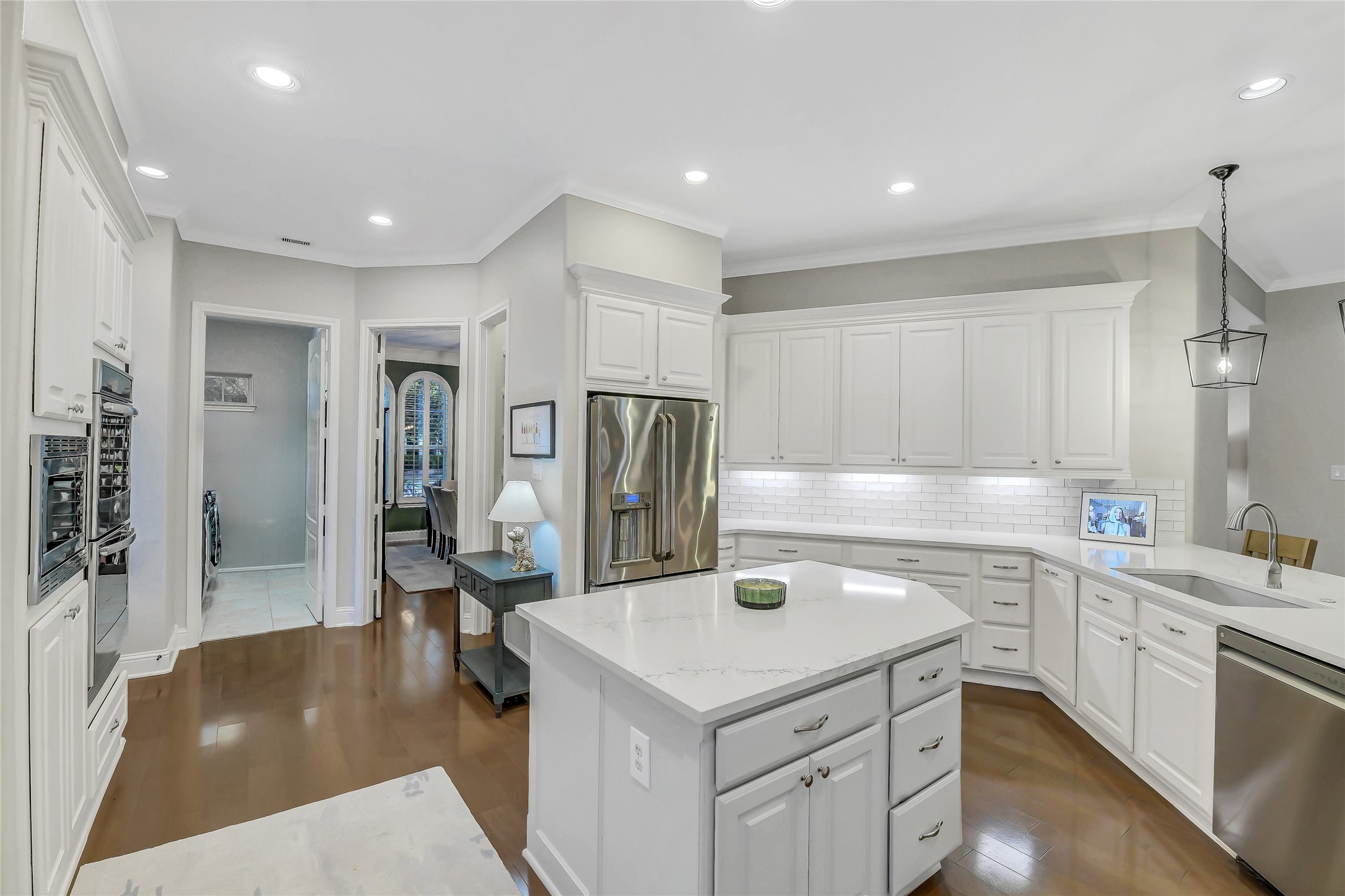 This bright, open-concept kitchen features an oversized quartz island, abundant custom cabinetry, stainless steel appliances, and a timeless white subway tile backsplash. Designed for both everyday living and entertaining, the spacious layout offers ample prep space, generous storage, and seamless flow into the surrounding living areas.