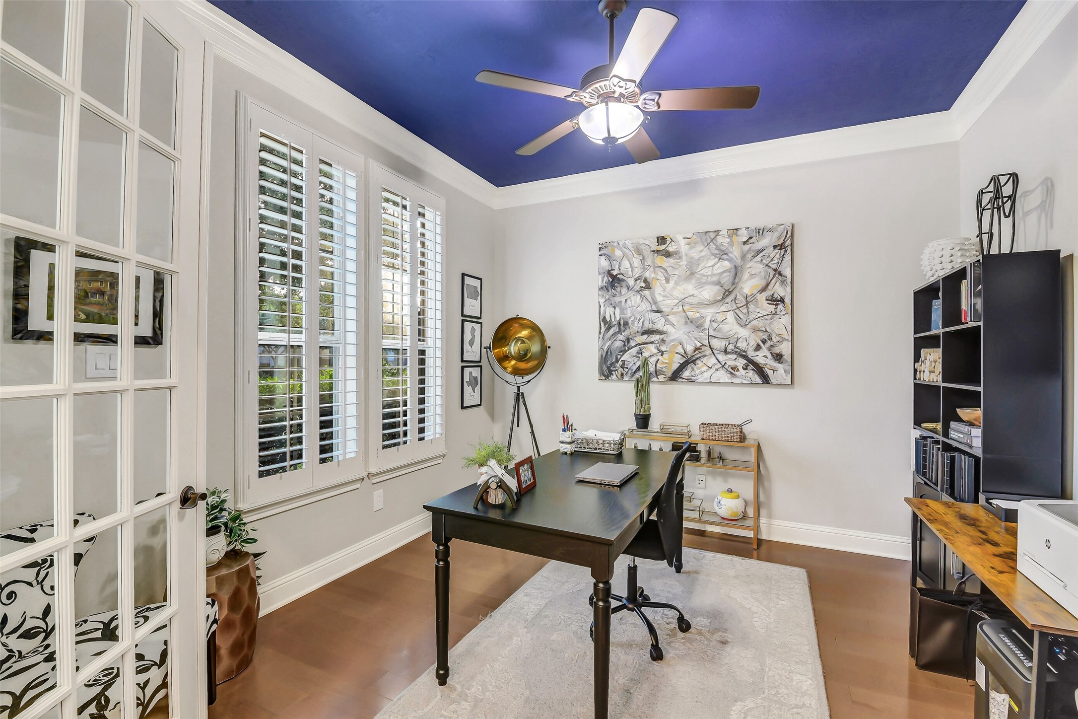 Light-filled private study enclosed by French doors, featuring plantation shutters, hardwood flooring, and an ideal layout for a home office or quiet workspace.