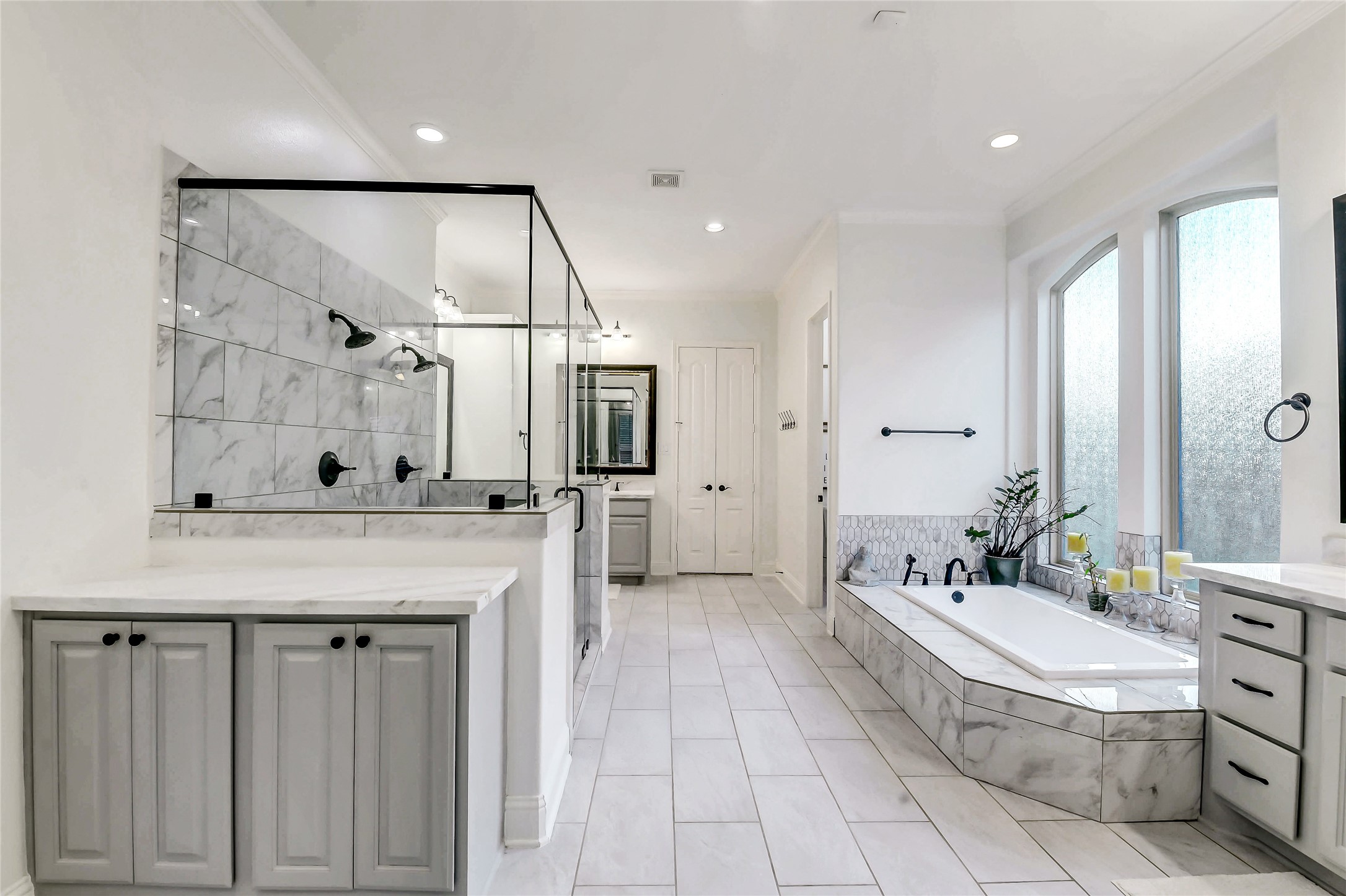 Indulge in a spa-inspired primary bath featuring separate vanities with dual sinks, an oversized walk-in shower with dual showerheads, and a luxurious soaking tub perfectly positioned for relaxation. Thoughtfully designed with a dedicated vanity area and separate his-and-her walk-in closets, this elegant retreat offers exceptional comfort, functionality, and abundant storage.