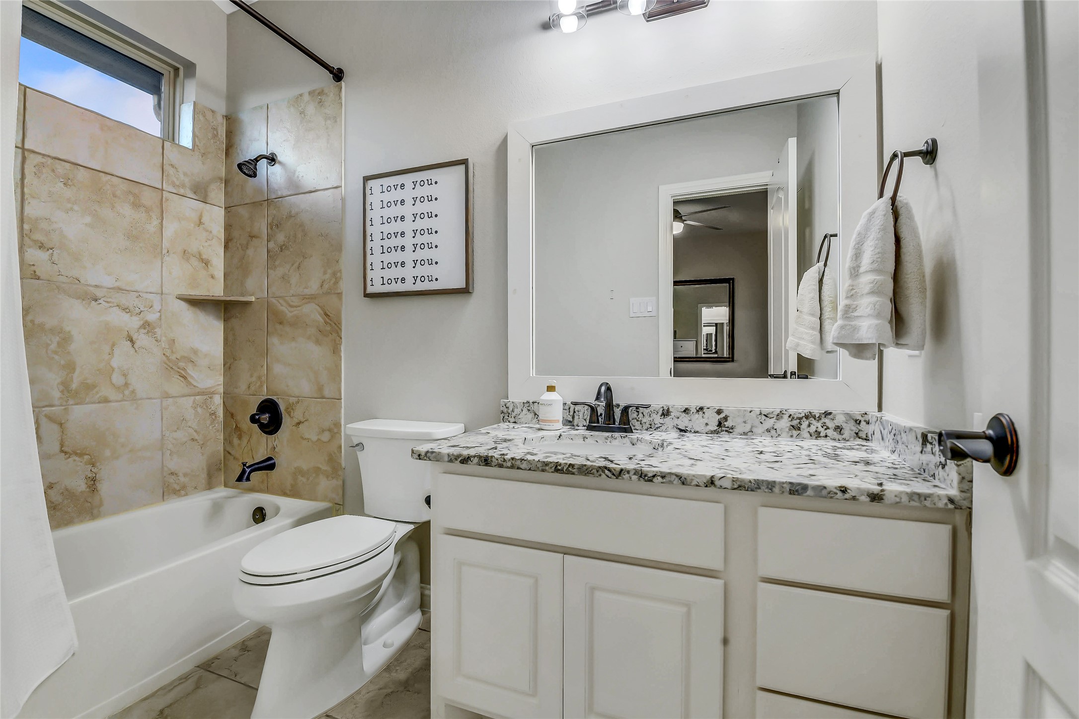 Private ensuite bathroom features a granite vanity, tiled tub/shower combination with a window for natural light, and stylish finishes.