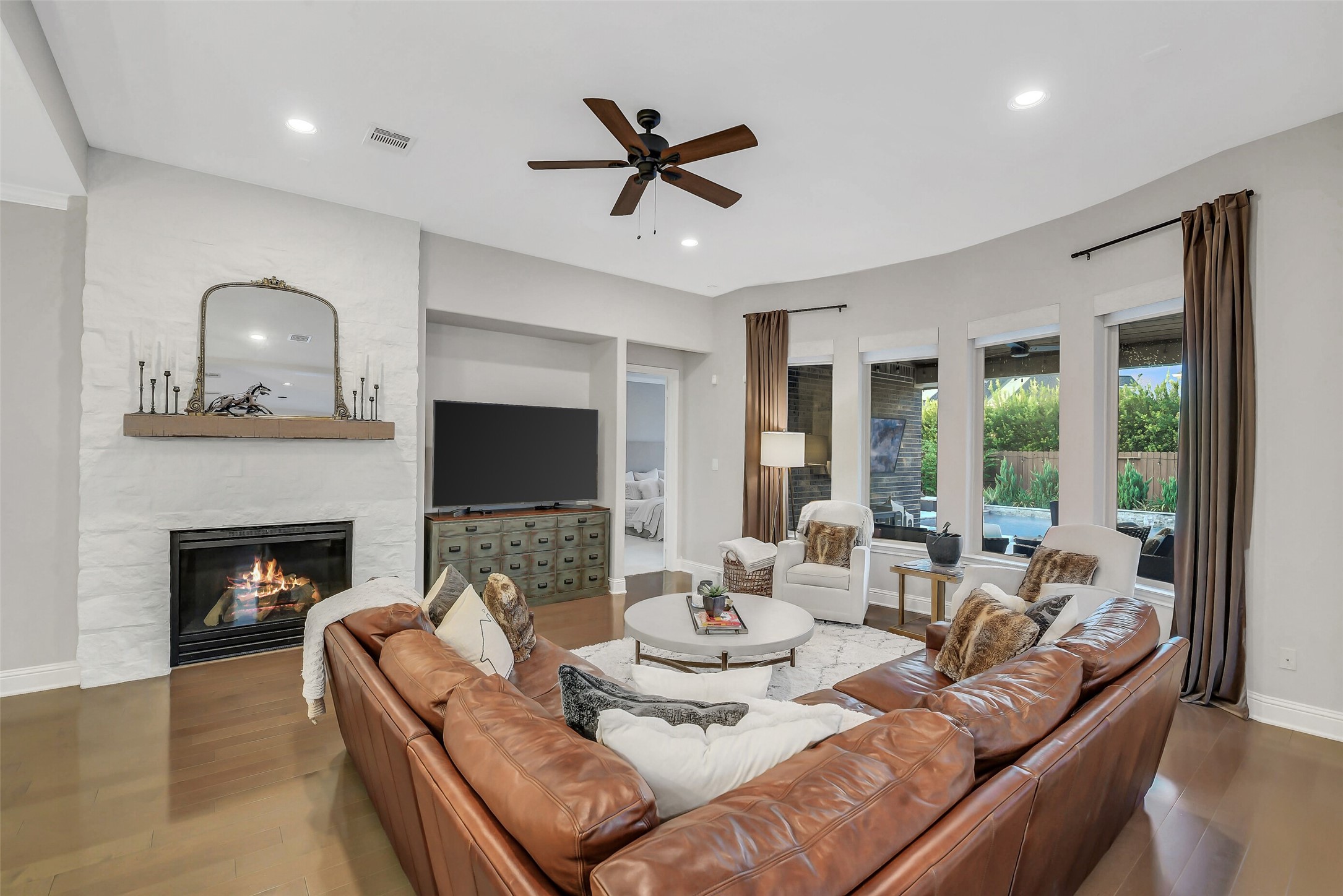 The welcoming family room features a dramatic stone fireplace and expansive windows overlooking the serene backyard retreat.
