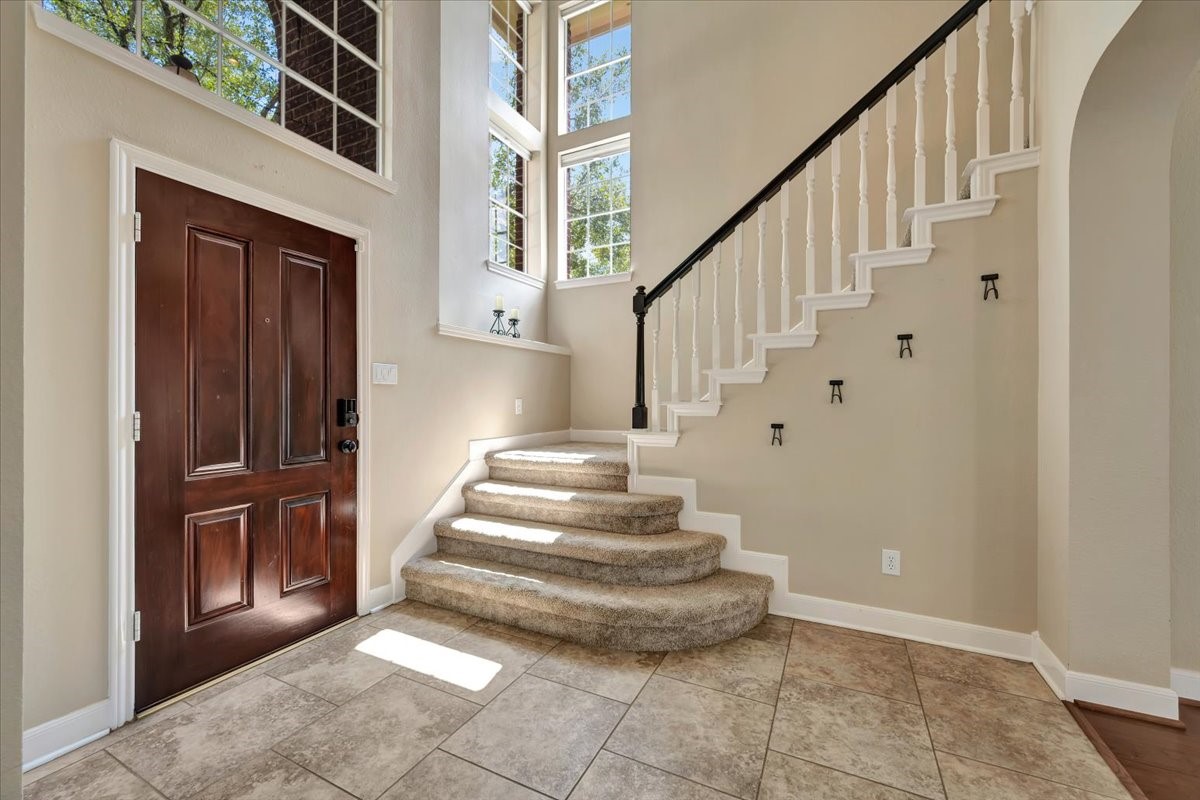 Bright two-story formal entry featuring a beautiful wood front door and a striking staircase leading upstairs.
