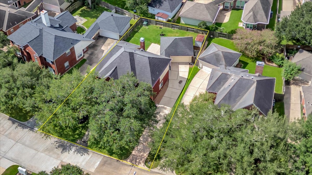 Alternate aerial view highlighting mature front-yard trees, shaded outdoor space, and the driveway leading to the detached garage.