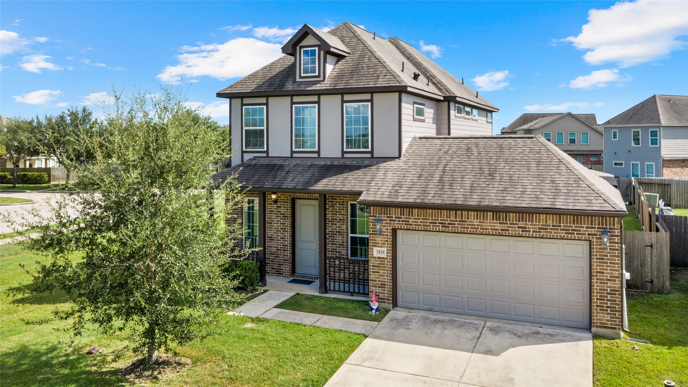 Charming two-story home featuring a brick exterior, garage, and lush front yard on a corner lot.