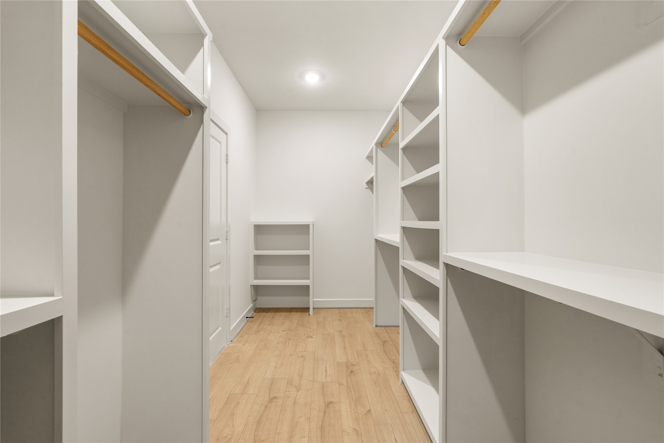 Expansive primary walk-in closet  custom built-in shelving towers, shoe racks, and dual hanging rods set over warm wood-look floors.