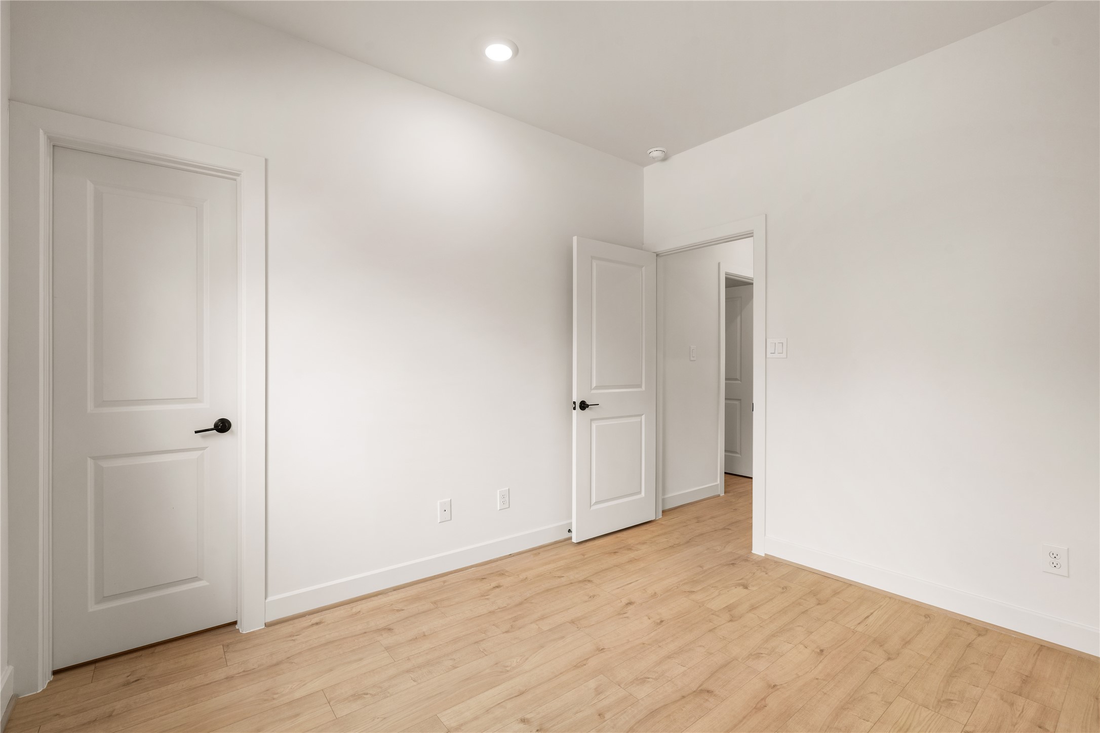 Bright guest bedroom perspective  smooth interior doors with matte black hardware, recessed lighting, and easy traffic flow to the hallway.