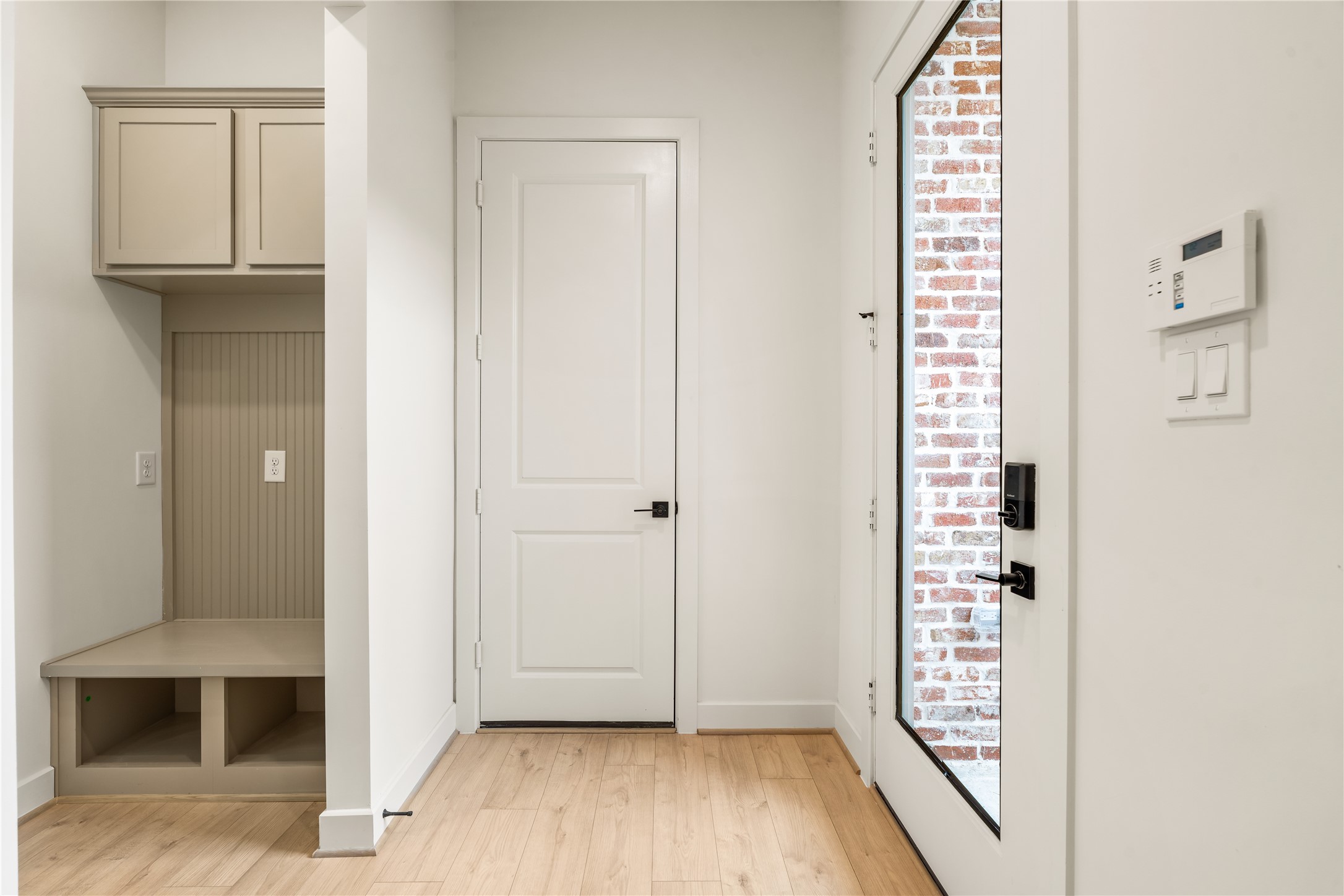Thoughtful mudroom drop zone  custom built-in bench seating, storage cubbies, upper cabinets, and glass-paneled front entry door.
