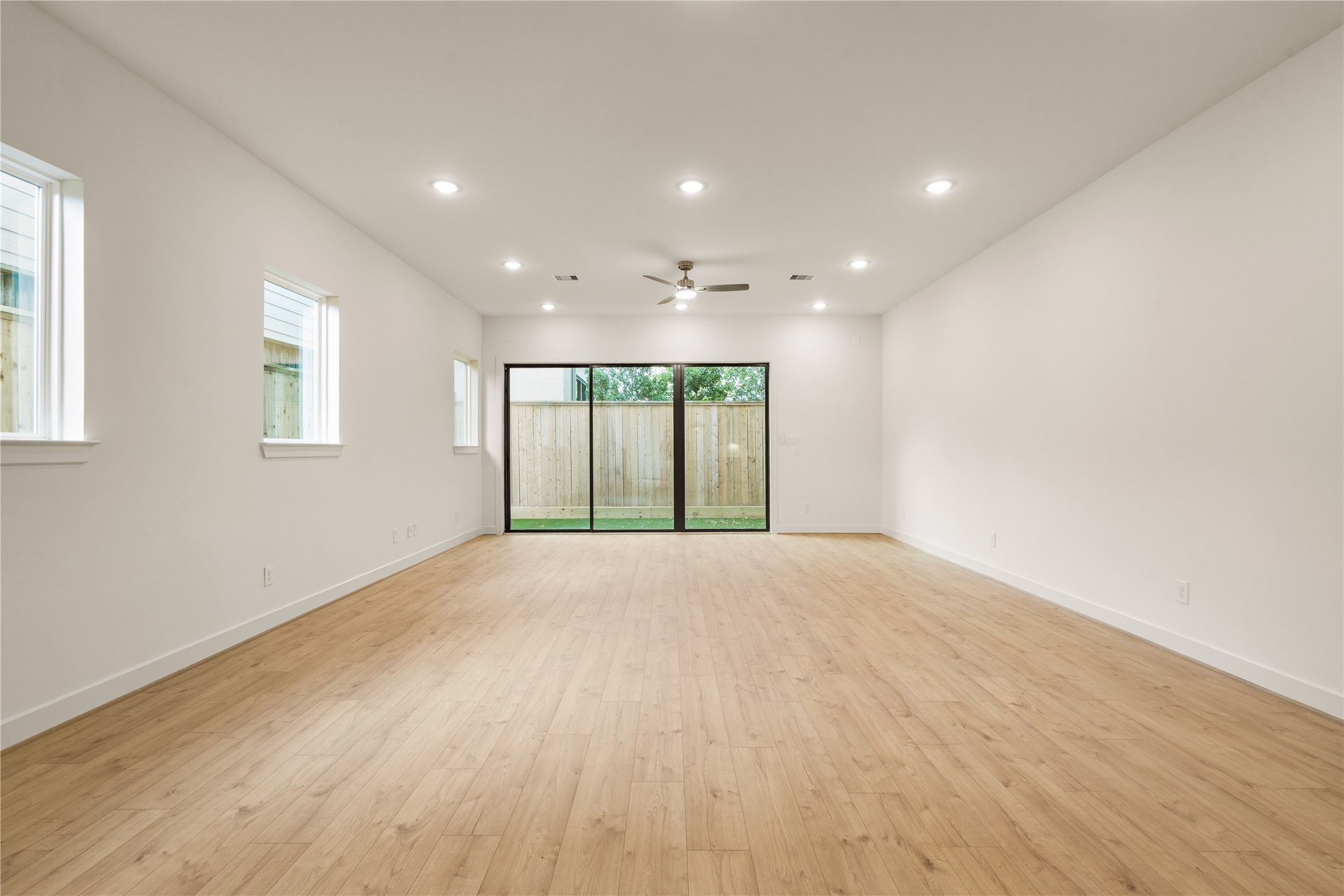 Spacious main living hall  wall-to-wall oak-look flooring, recessed LED lighting throughout, side-yard accent windows, and oversized glass sliding doors opening to the backyard.
