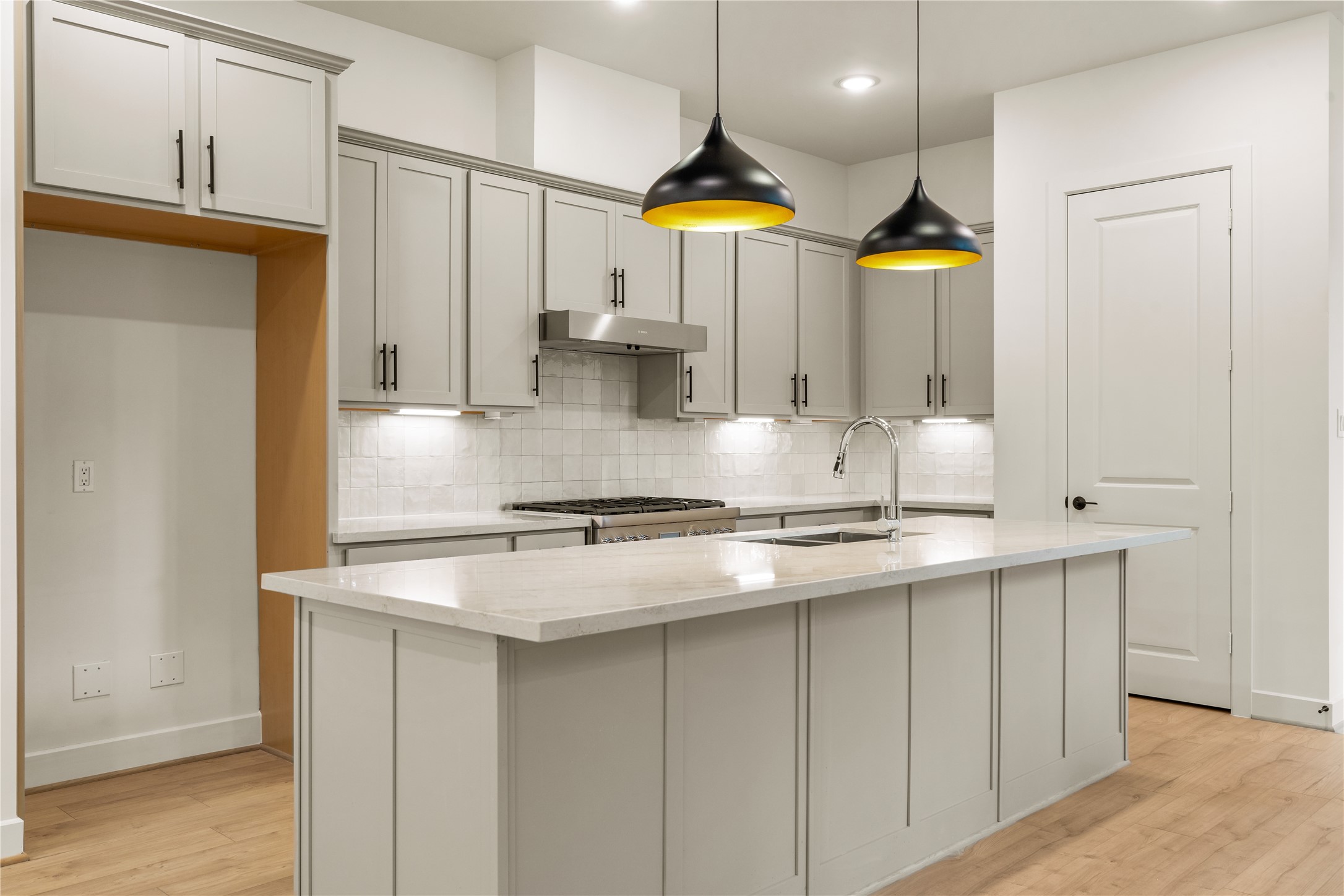 Gourmet workspace layout  sleek gooseneck faucet, warm light-wood flooring, and custom cabinetry with dedicated refrigerator alcove.