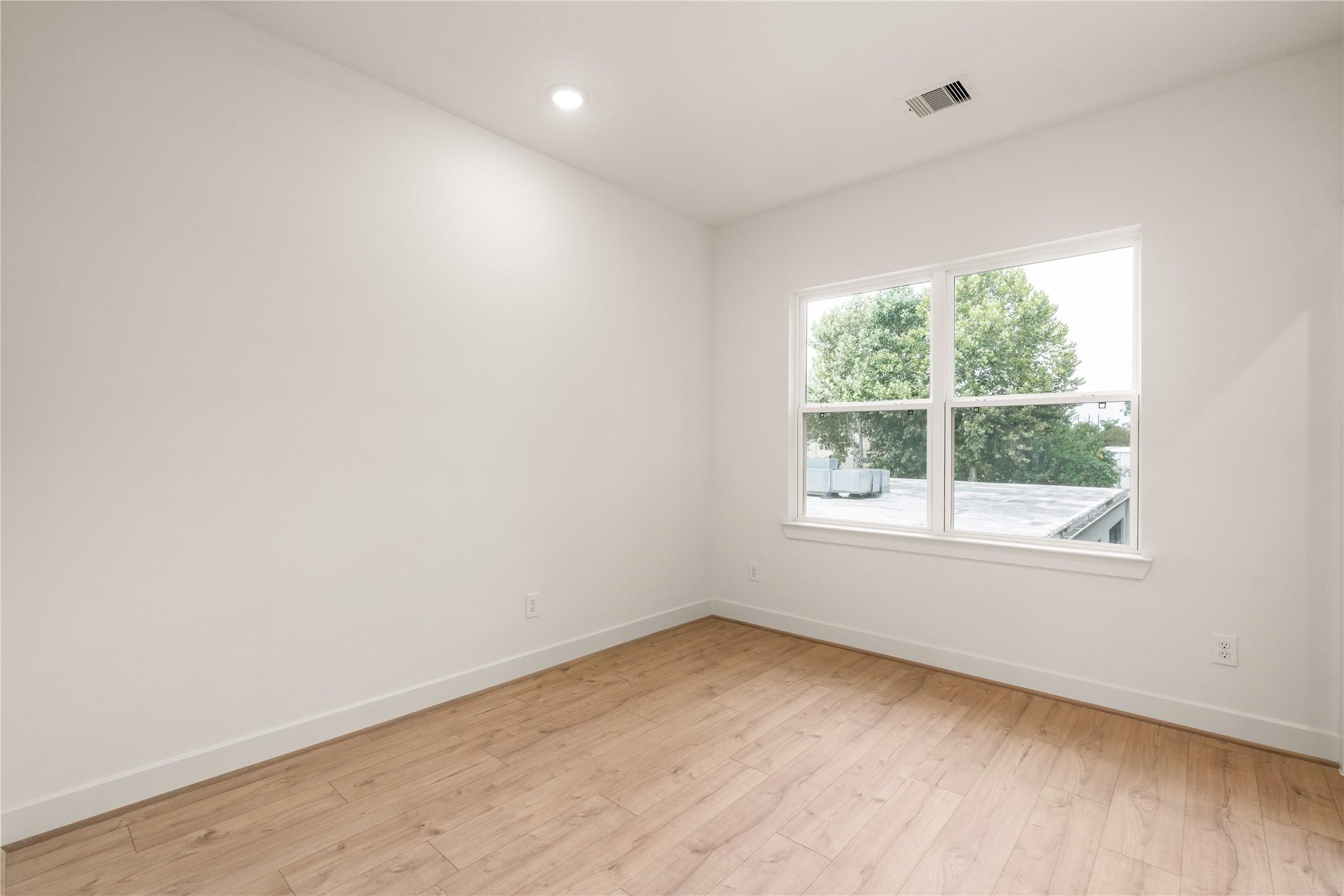 Secondary bedroom  light-filled layout with large picture window, wide-plank wood-look flooring, and crisp modern trim.