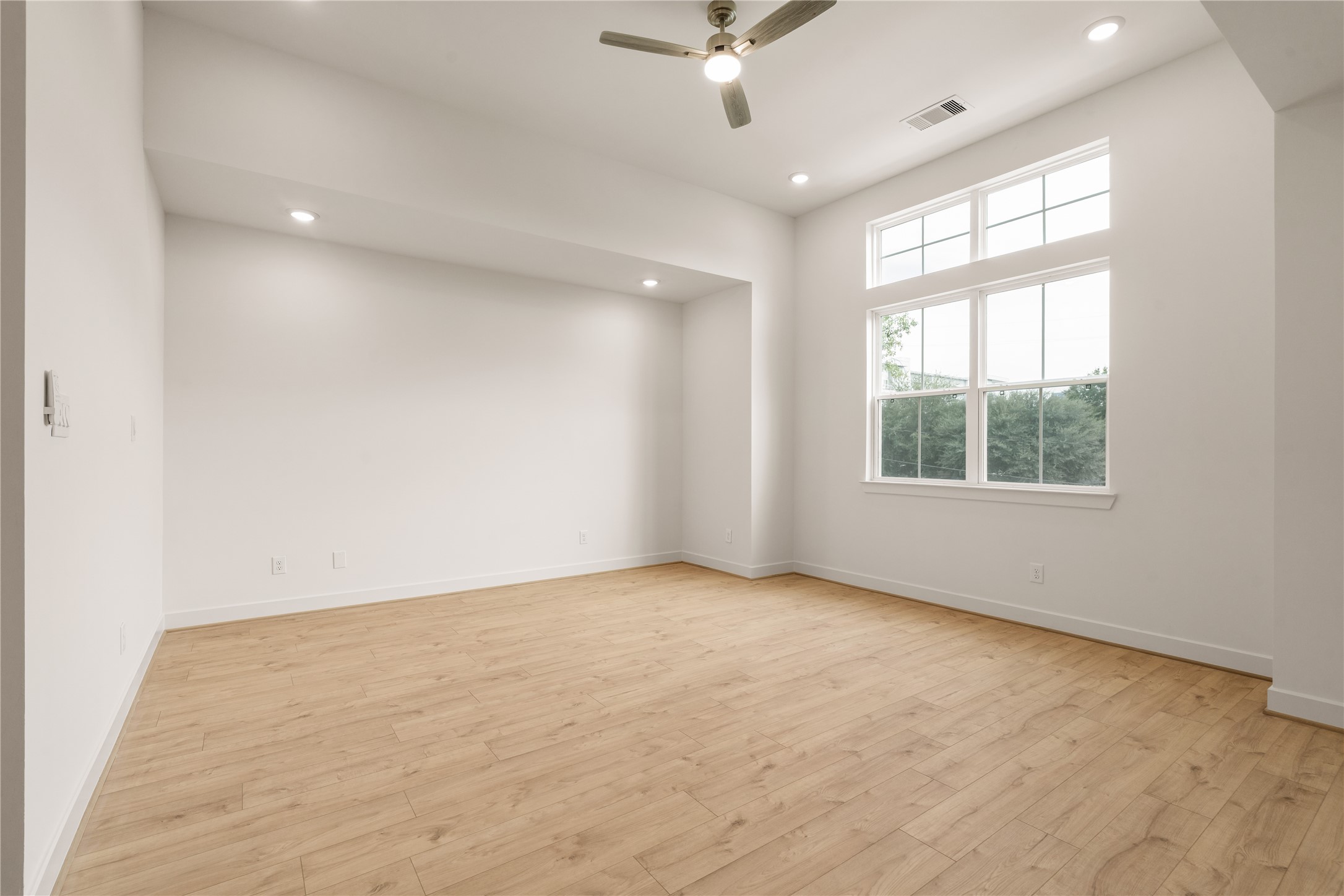 Primary bedroom sanctuary  soaring high ceiling with transom windows streaming morning light, recessed lighting, and modern ceiling fan.