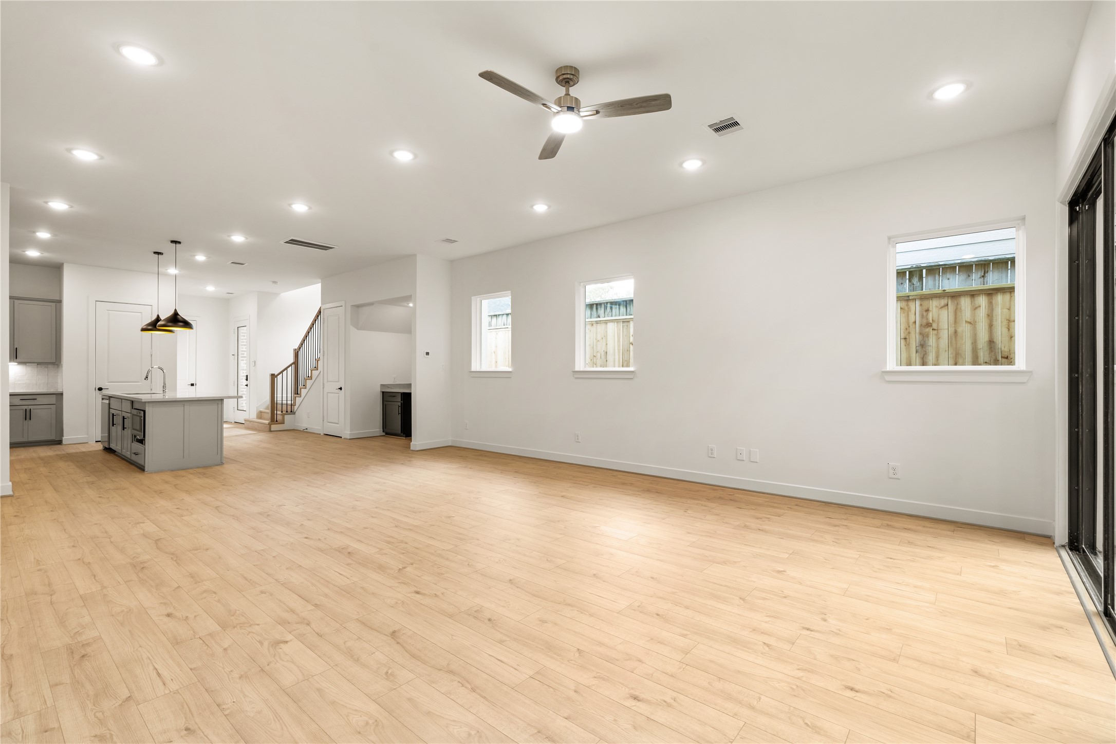 Generous living hall perspective  bright neutral walls, side-yard accent windows, and clear sightlines to the stairwell and kitchen hub.