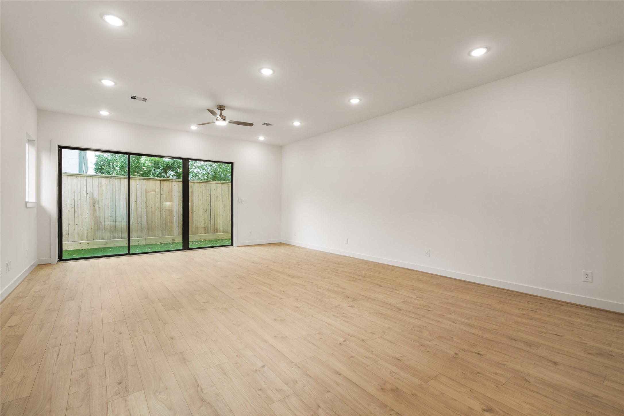 Sunlit living retreat  floor-to-ceiling multi-slide glass doors opening directly to the private yard, framed by warm wood flooring and recessed LED lighting.