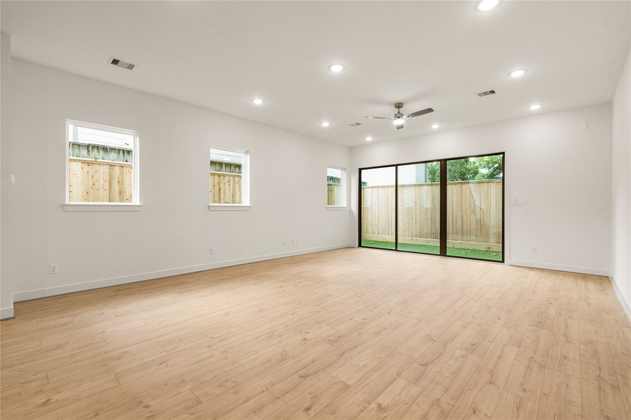 Expansive open living space  continuous oak-look flooring, multiple side windows providing balanced natural light, and modern ceiling fan detail.