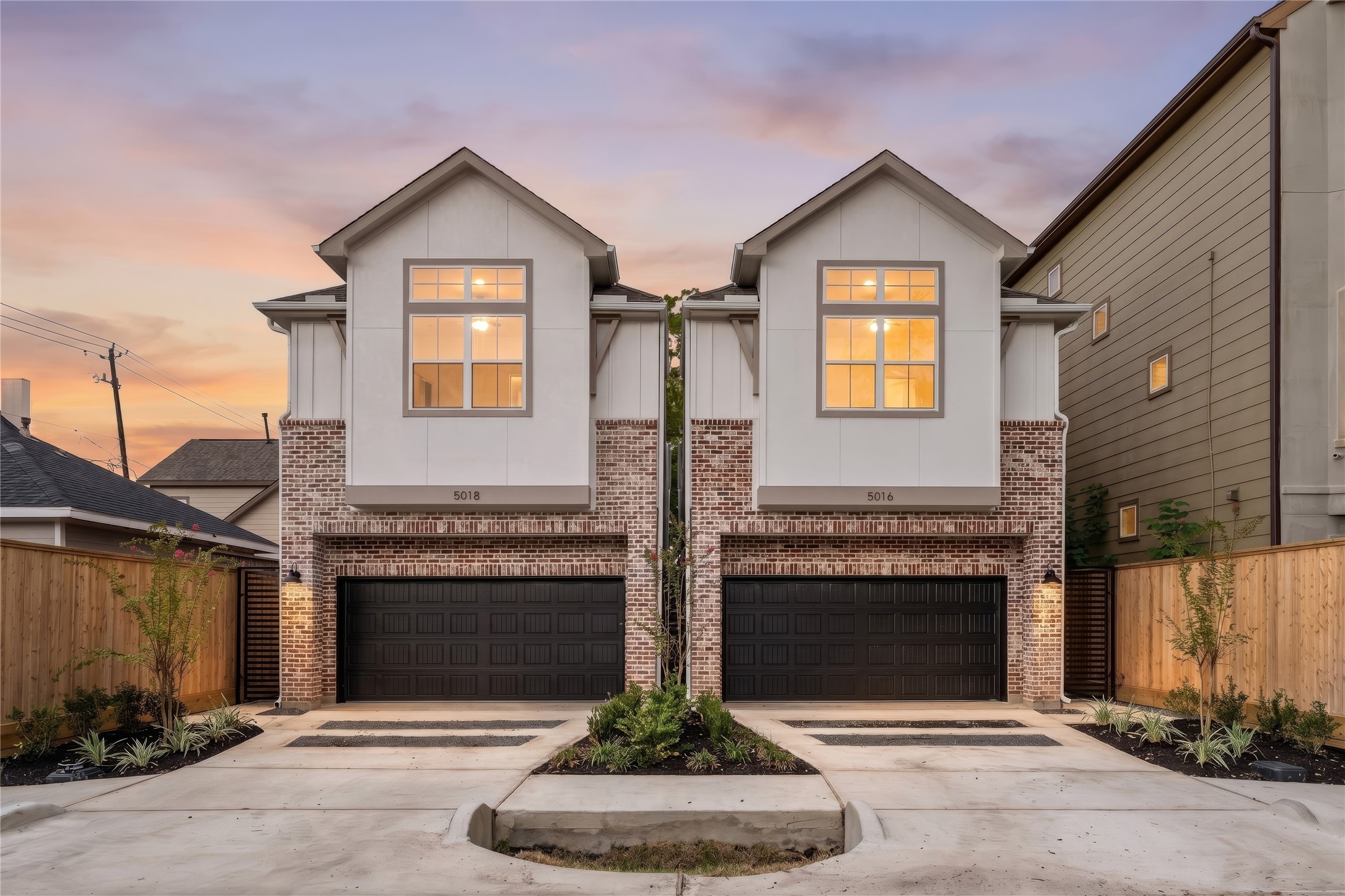 Stunning sunset elevation  classic brick lower facade paired with clean board-and-batten upper gables, dark garage doors, and manicured entryway landscaping.