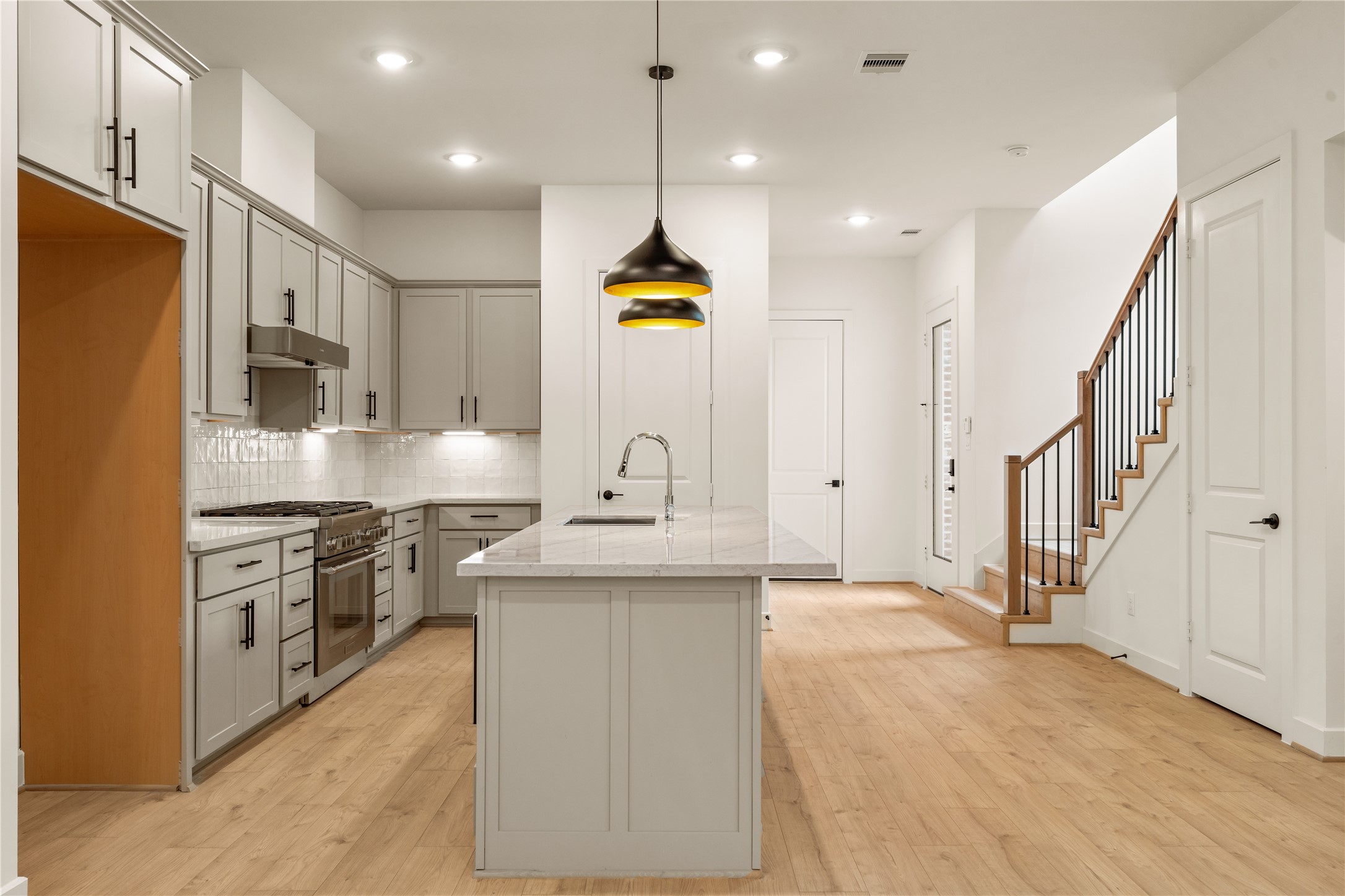 Heart of the main level  centered island prep station, wide-plank oak flooring, and direct sightlines to the stair run and entry foyer.