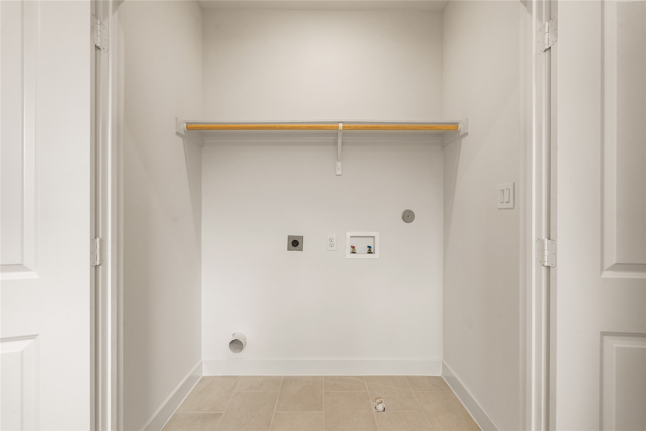 Upper-level laundry nook  dedicated tiled closet space equipped with built-in storage shelf and hanging clothes rod.