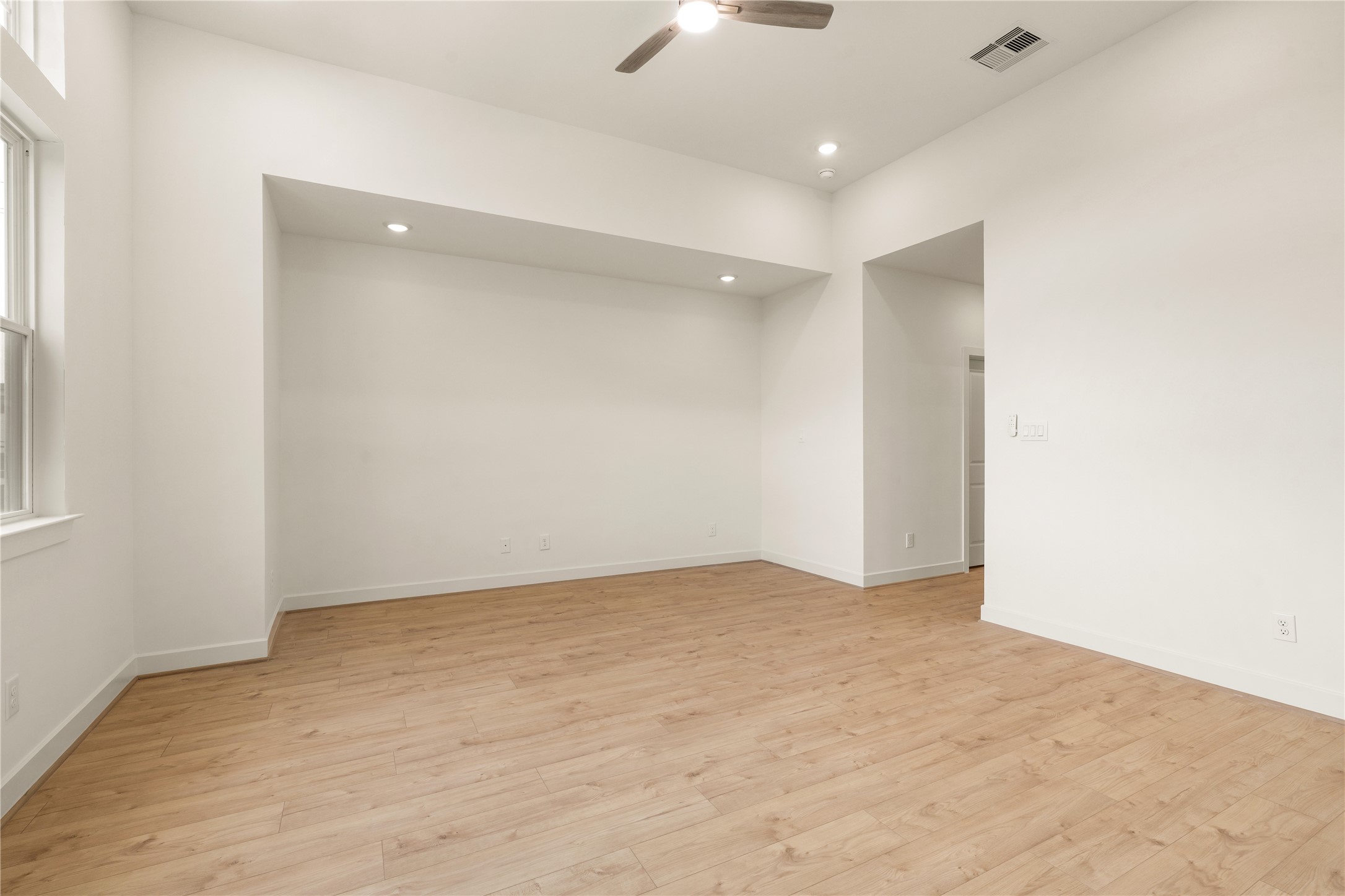 Expansive primary bedroom layout  clean neutral walls, recessed lighting, ceiling fan detail, and direct access to the ensuite bath.