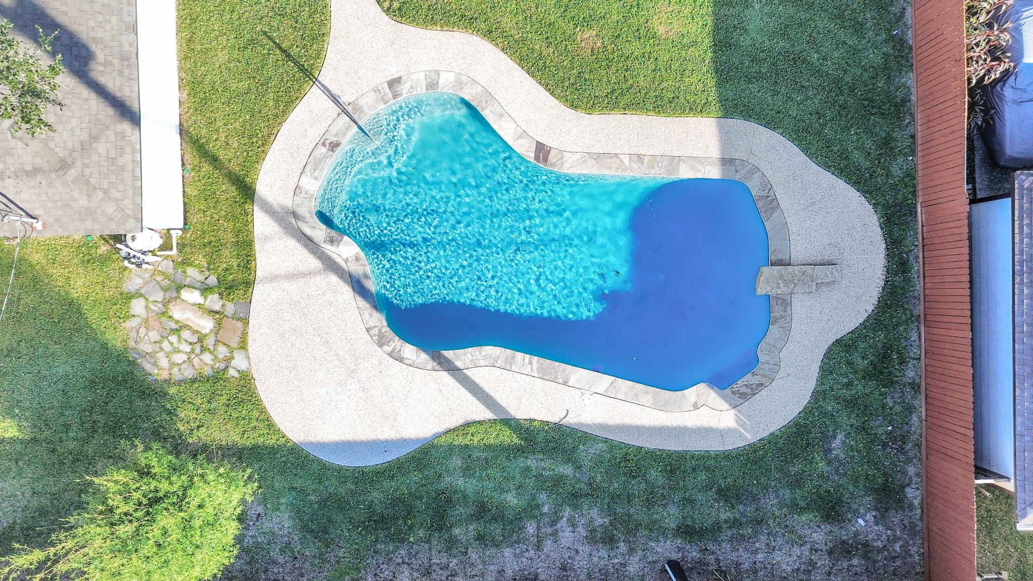 An aerial view showcases the magnificent pool, surrounded by elegant stone coping and featuring a unique stone diving board, creating a striking focal point in the backyard. Just in time for summertime!