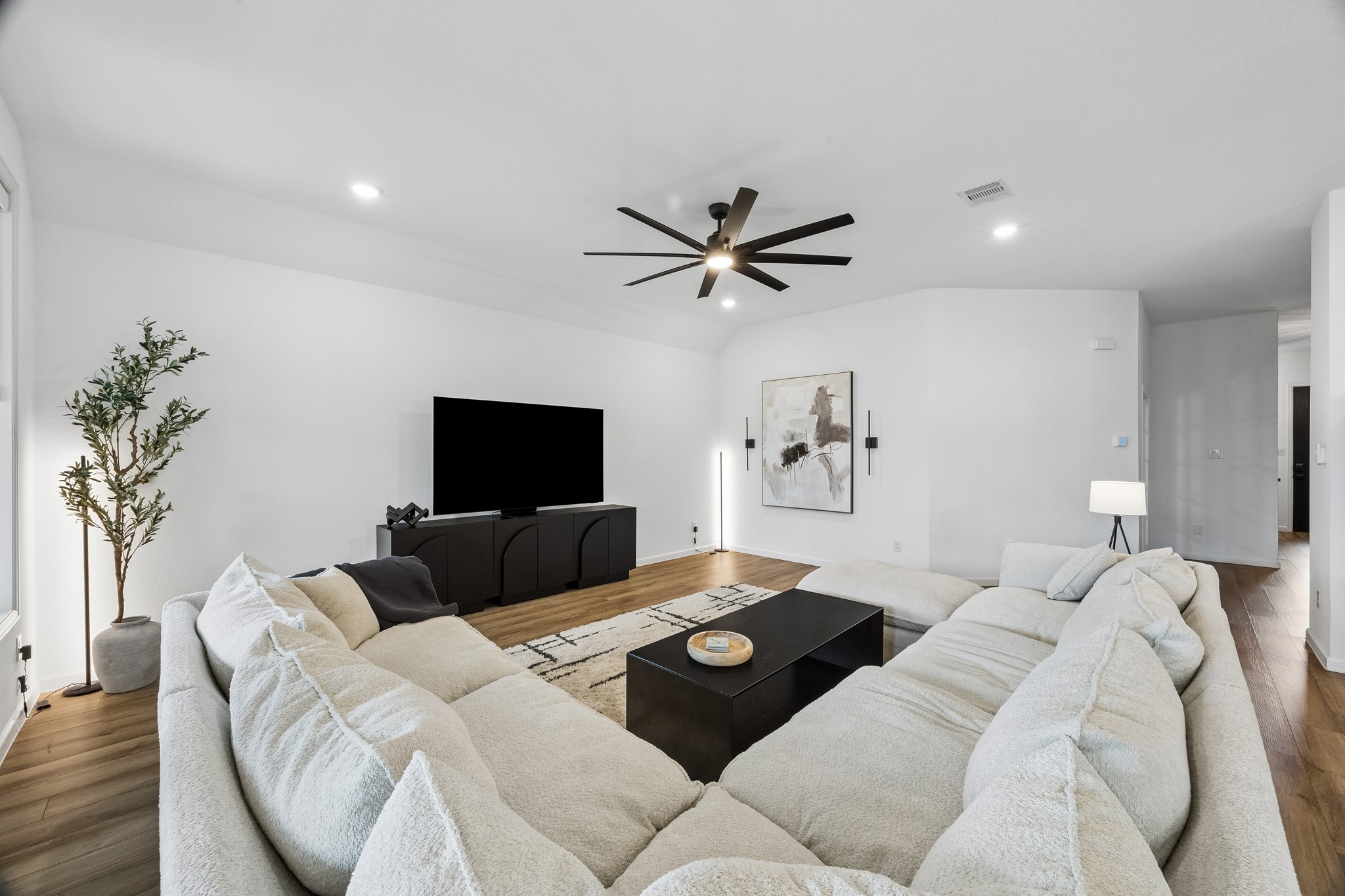 The living room is open and spacious. A oversized fan and automatic shades stand out in this elegant space.