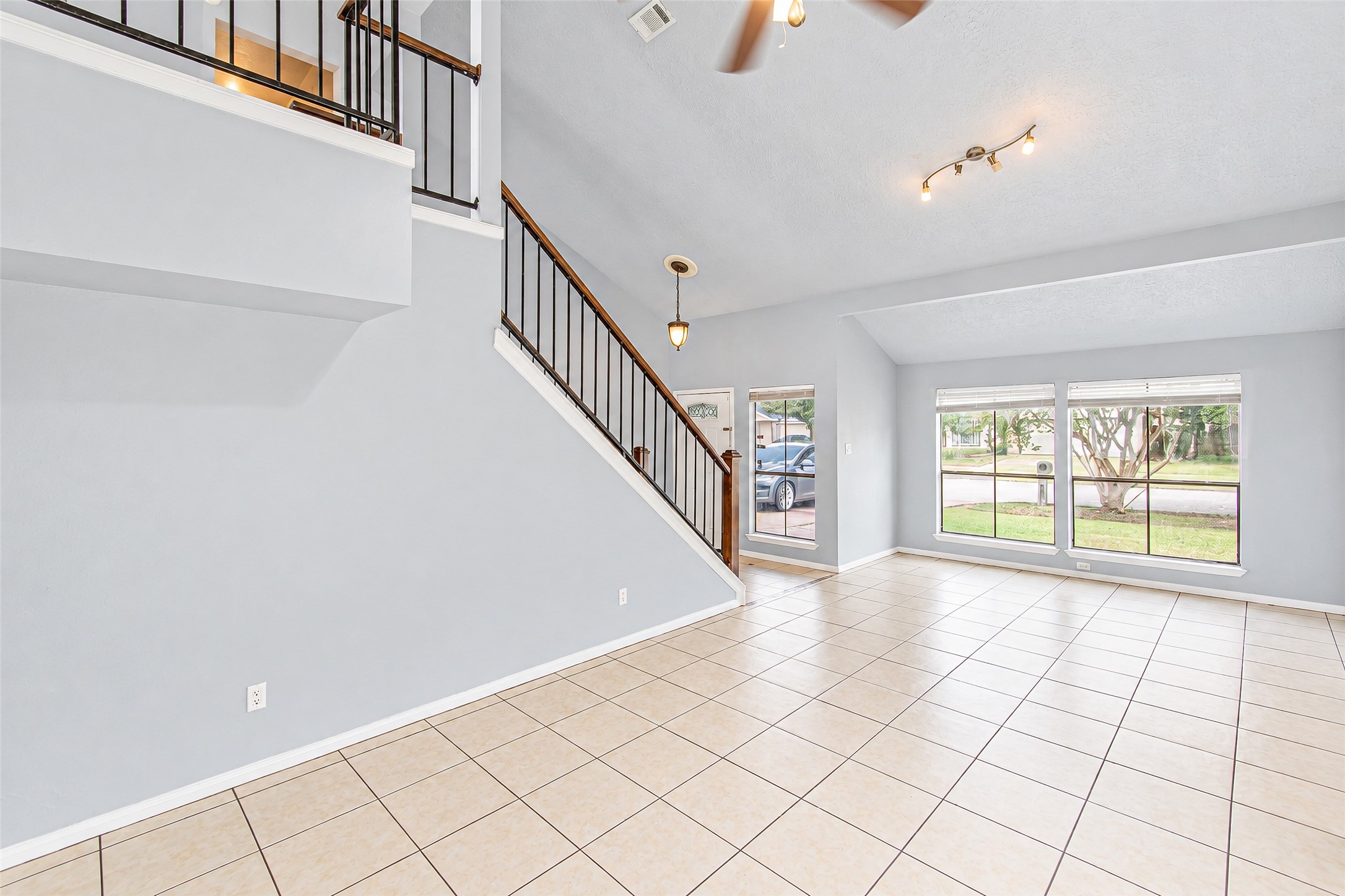 Spacious living area with high ceilings and large windows offering abundant natural light, complemented by a modern staircase and tiled flooring. Spacious living area with high ceilings and large windows offering abundant natural light, complemented by a modern staircase and tiled flooring.