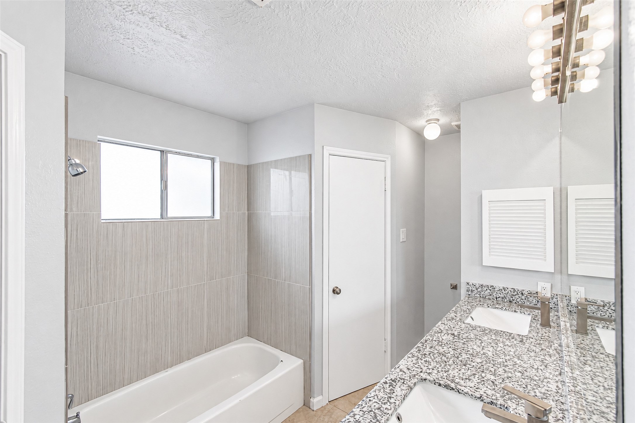 Bright and modern bathroom featuring a stylish granite countertop, sleek fixtures, and a spacious bathtub with contemporary tile surround.