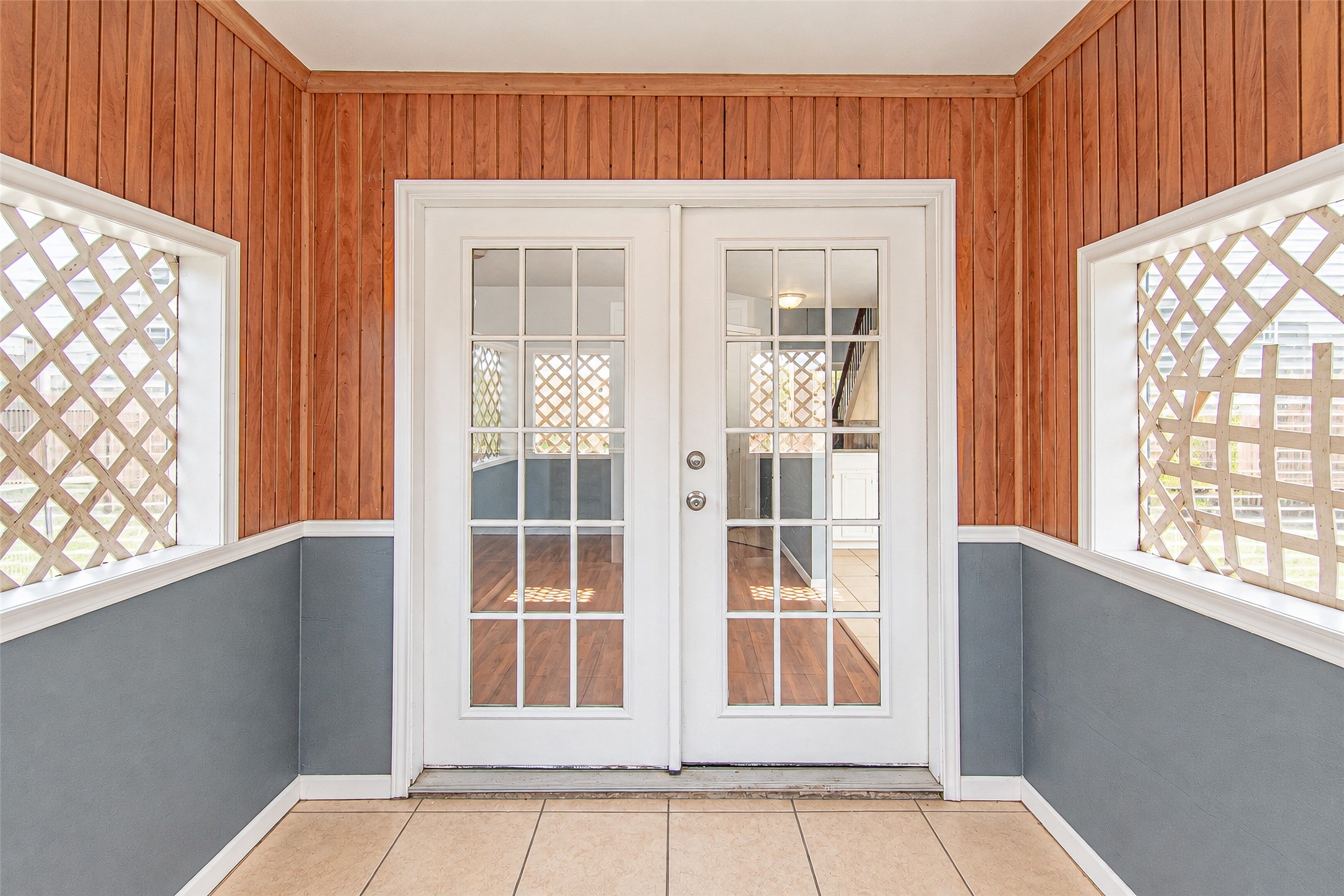 Charming sunroom with warm wood paneling and elegant French doors, offering a cozy transition to the interior living space.