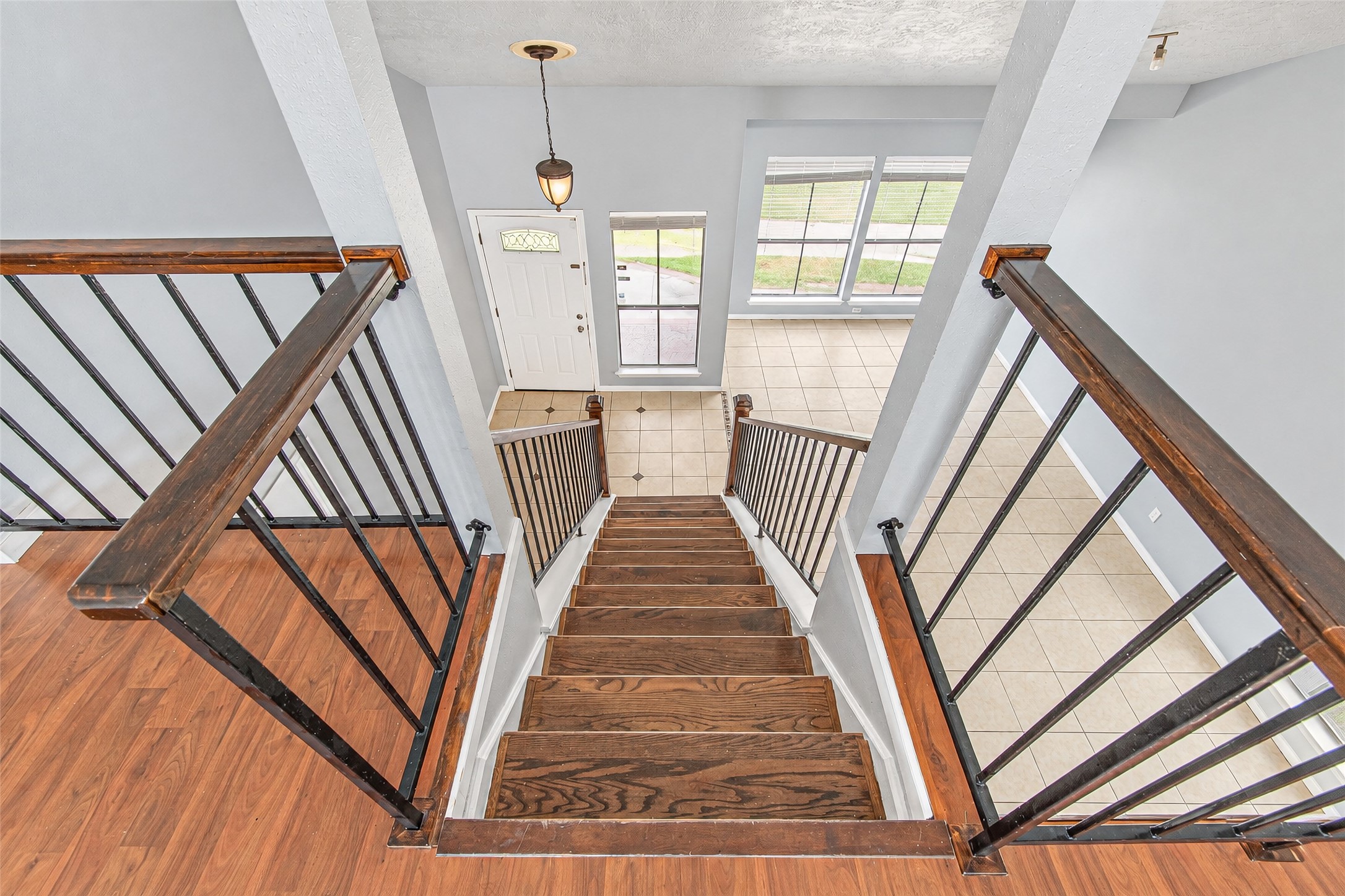 Elegant staircase with rich wood steps and sleek black railings leads to a bright foyer with large windows and tile flooring.