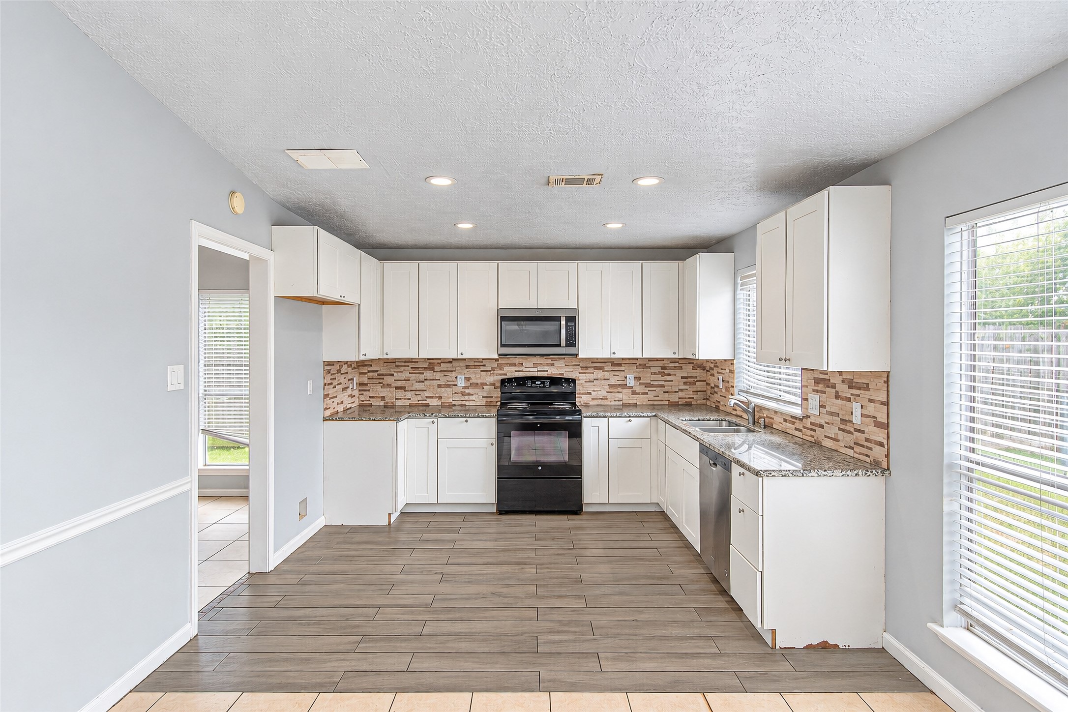 Bright and modern kitchen featuring sleek white cabinetry, granite countertops, and a stylish tile backsplash, with ample natural light streaming through large windows.