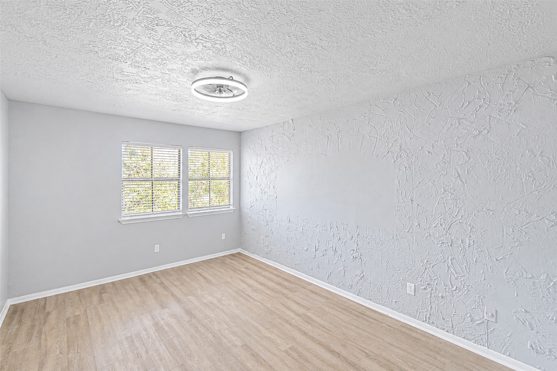 Bright and airy room featuring textured walls, large windows for ample natural light, and elegant wood-look flooring.