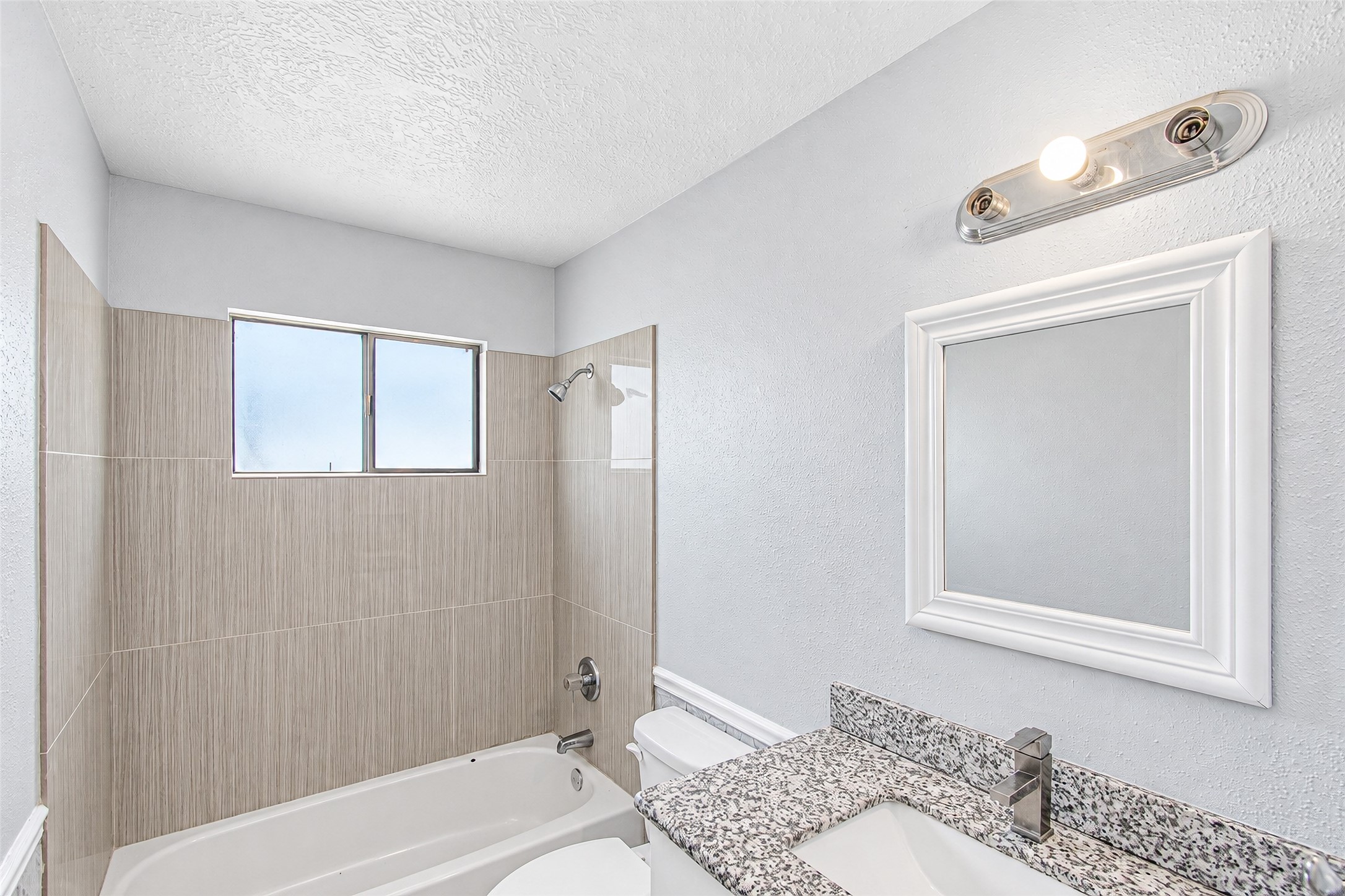 Bright and modern bathroom featuring a sleek granite countertop, elegant tile backsplash, and a convenient shower-tub combo.