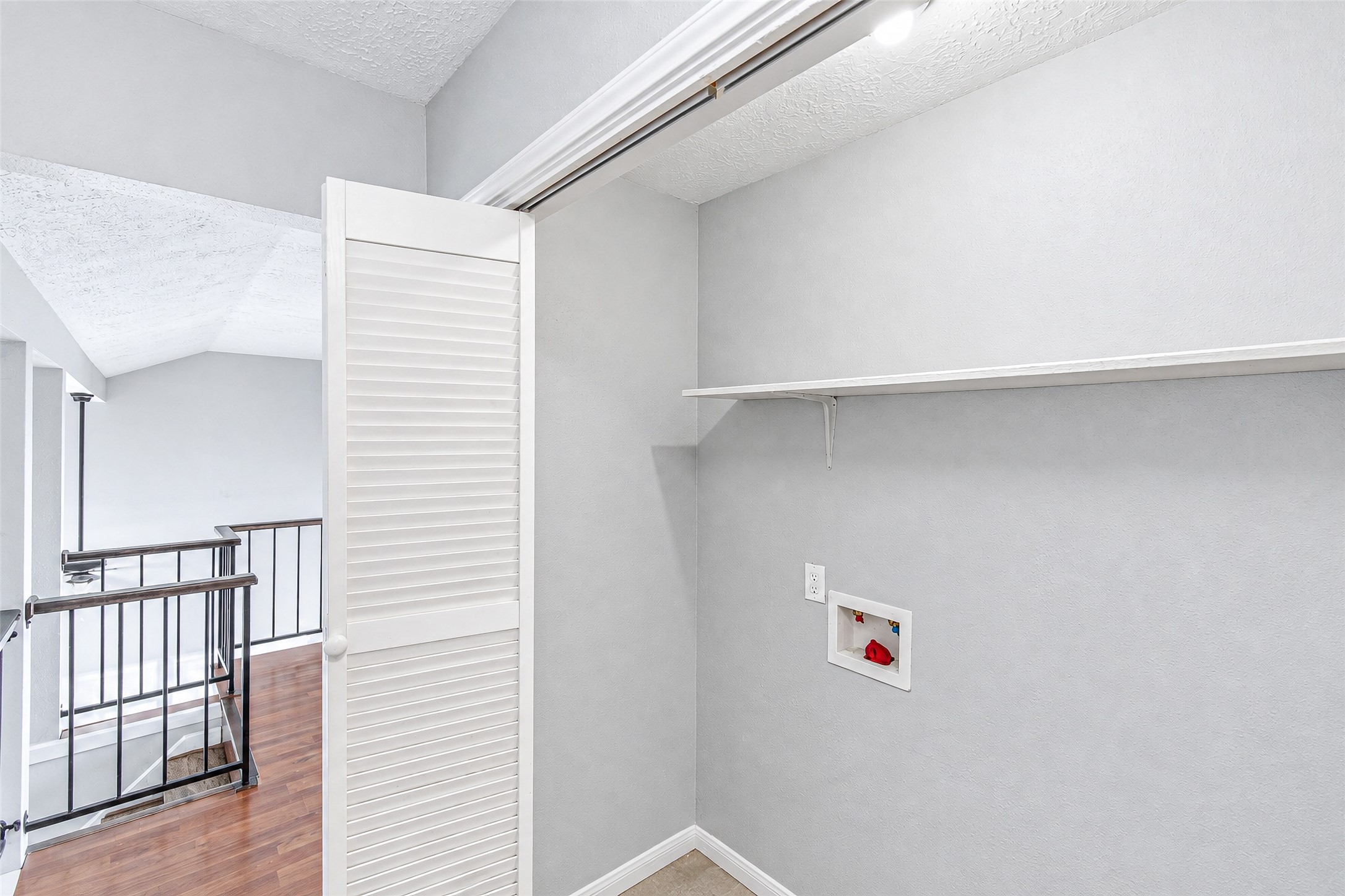 Convenient laundry nook with built-in shelving, located next to a stylish railing overlooking the lower level.