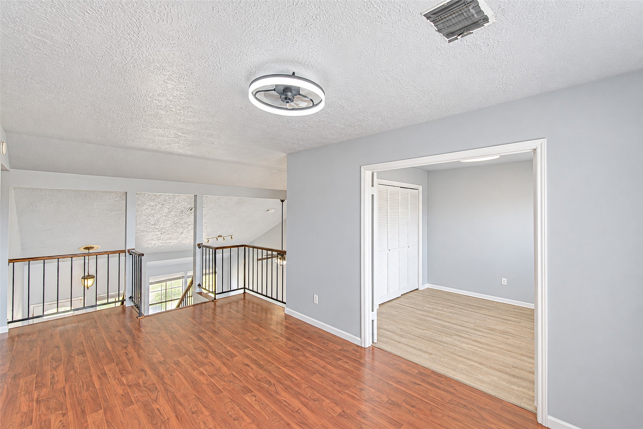 Bright and airy loft space with beautiful wood flooring, modern light fixture, and ample natural light from large windows, perfect for a cozy retreat or home office.