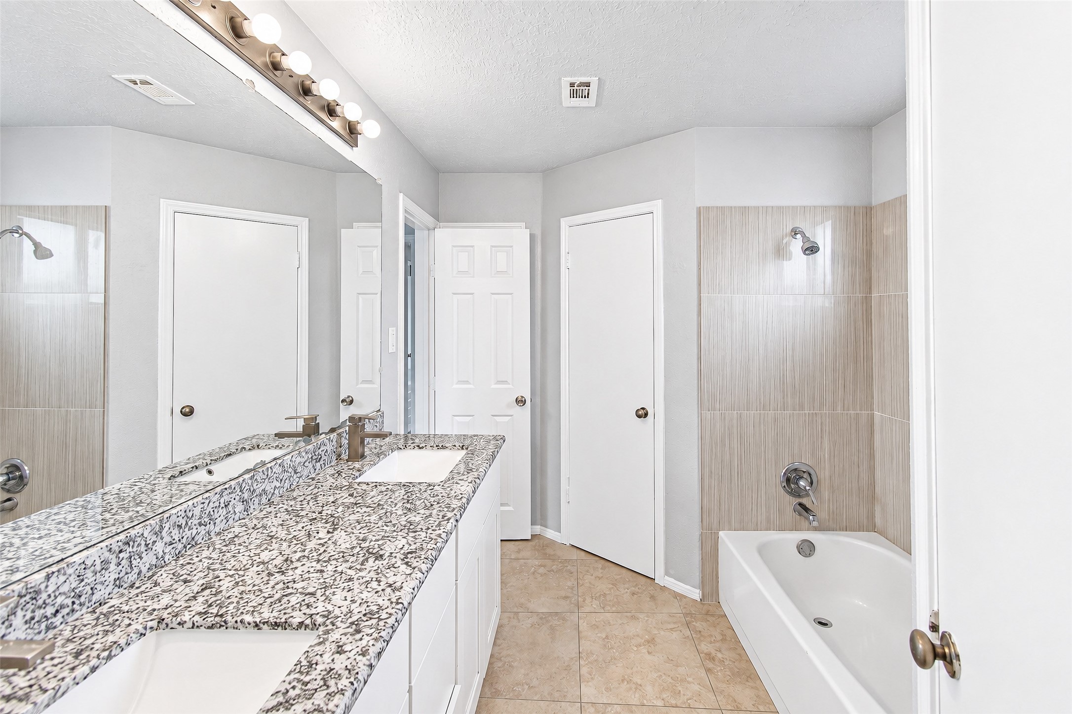 Bright and modern bathroom featuring a sleek granite countertop with dual sinks, a full bathtub with stylish tile surround, and ample lighting.