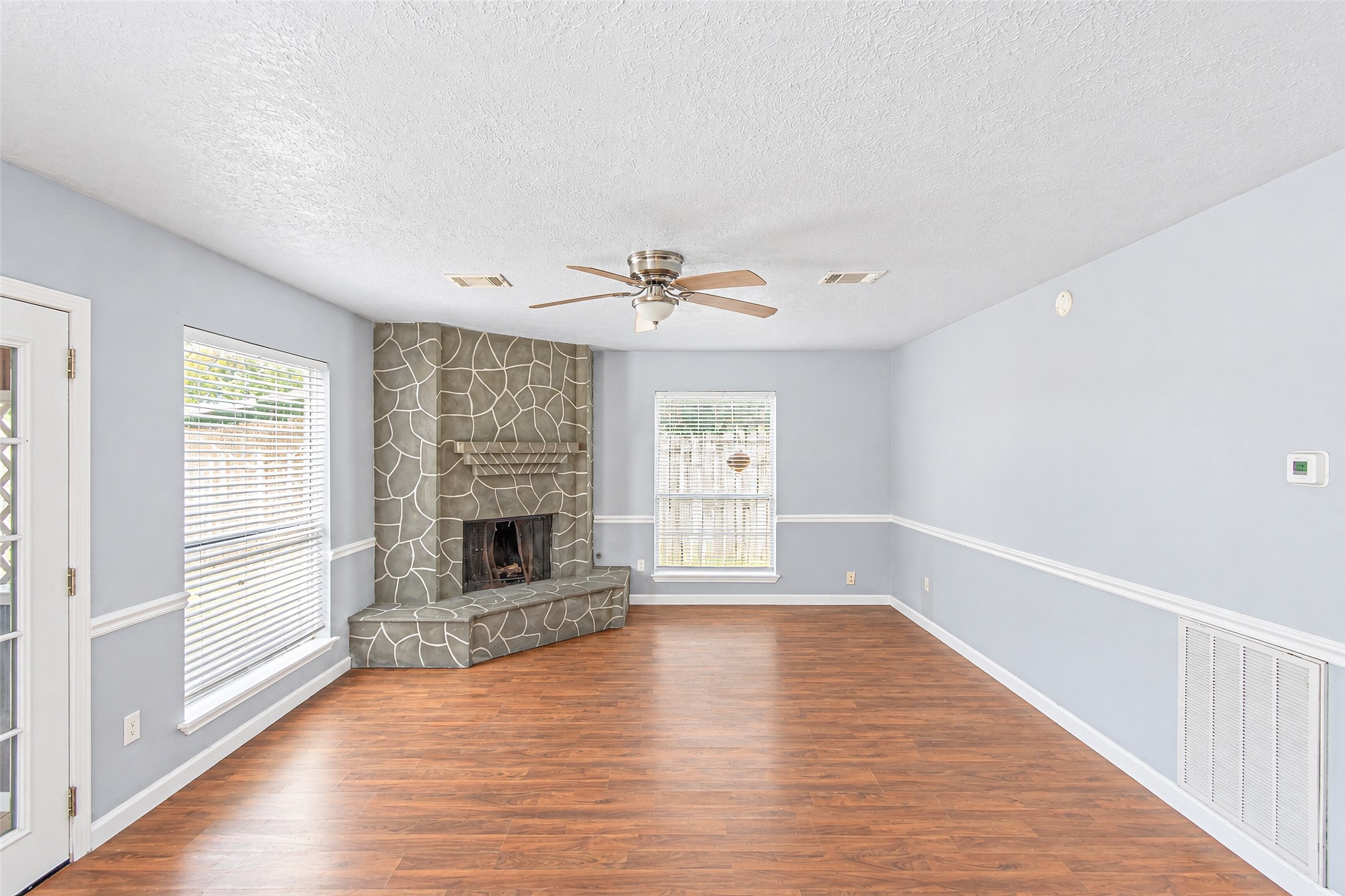 Bright and inviting living room featuring a unique stone fireplace, hardwood floors, and ample natural light from large windows.