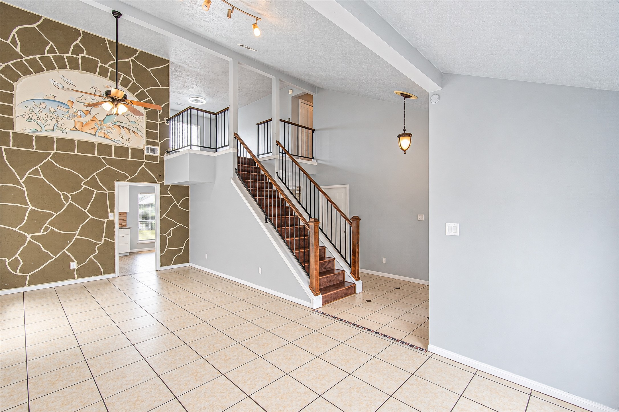 Spacious living area with high ceilings and a decorative accent wall, featuring a striking staircase with wooden steps and elegant railing, leading to the upper level. Spacious living area with high ceilings and a decorative accent wall, featuring a striking staircase with wooden steps and elegant railing, leading to the upper level.