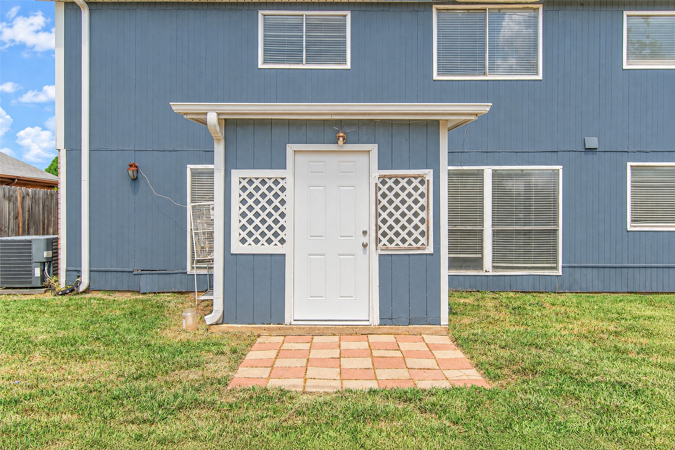 Charming blue exterior with a welcoming side entrance and lattice accents, complemented by a neatly paved walkway and a well-maintained lawn.