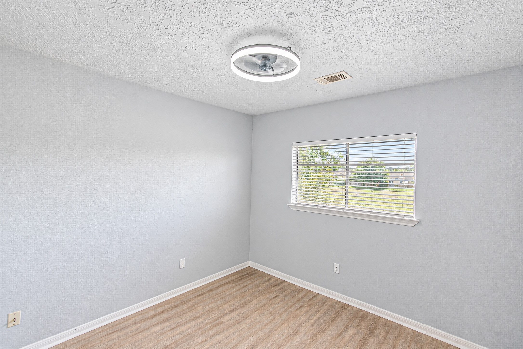 Bright and airy room featuring fresh neutral walls, a modern light fixture, and a large window offering natural light and views of the outdoors.