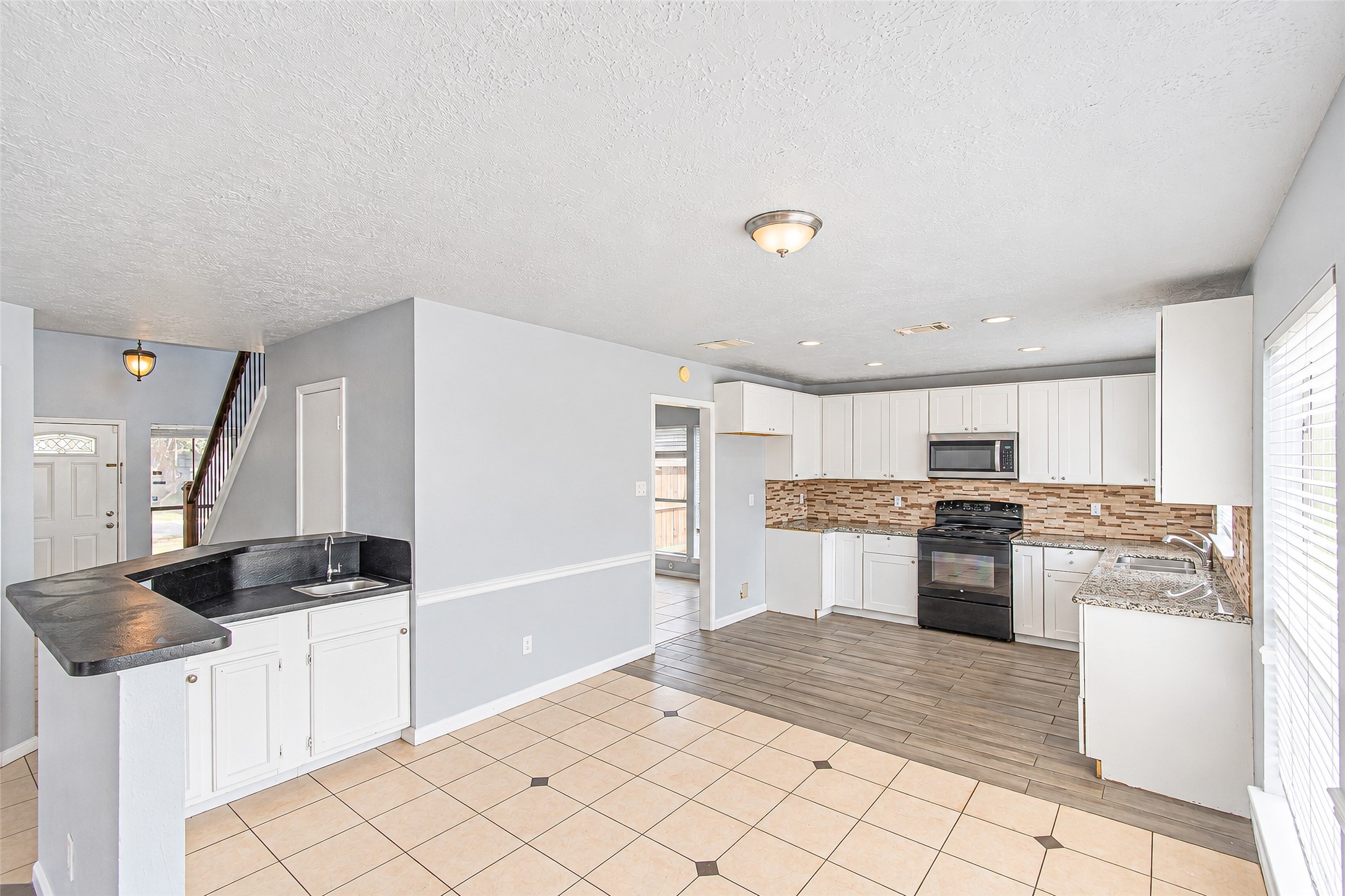 Bright and spacious kitchen features modern white cabinetry, sleek countertops, and a stylish tile backsplash, seamlessly flowing into an open-concept living area with abundant natural light.