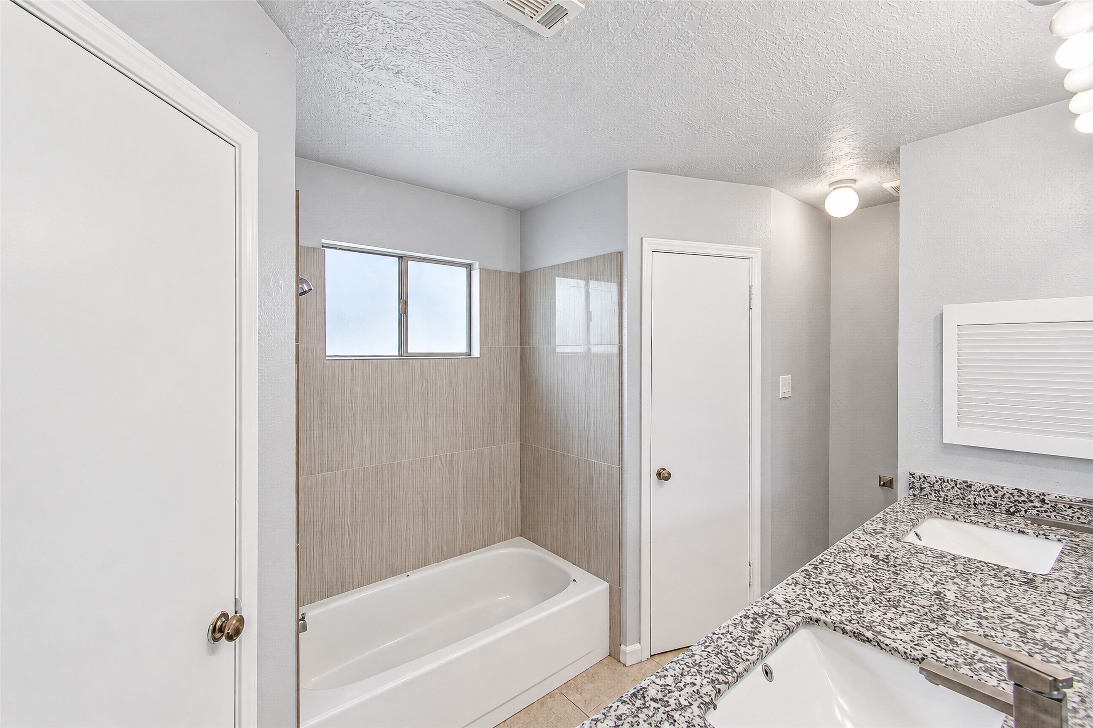 Bright and modern bathroom featuring a sleek granite countertop with dual sinks, a tiled bathtub, and ample lighting.