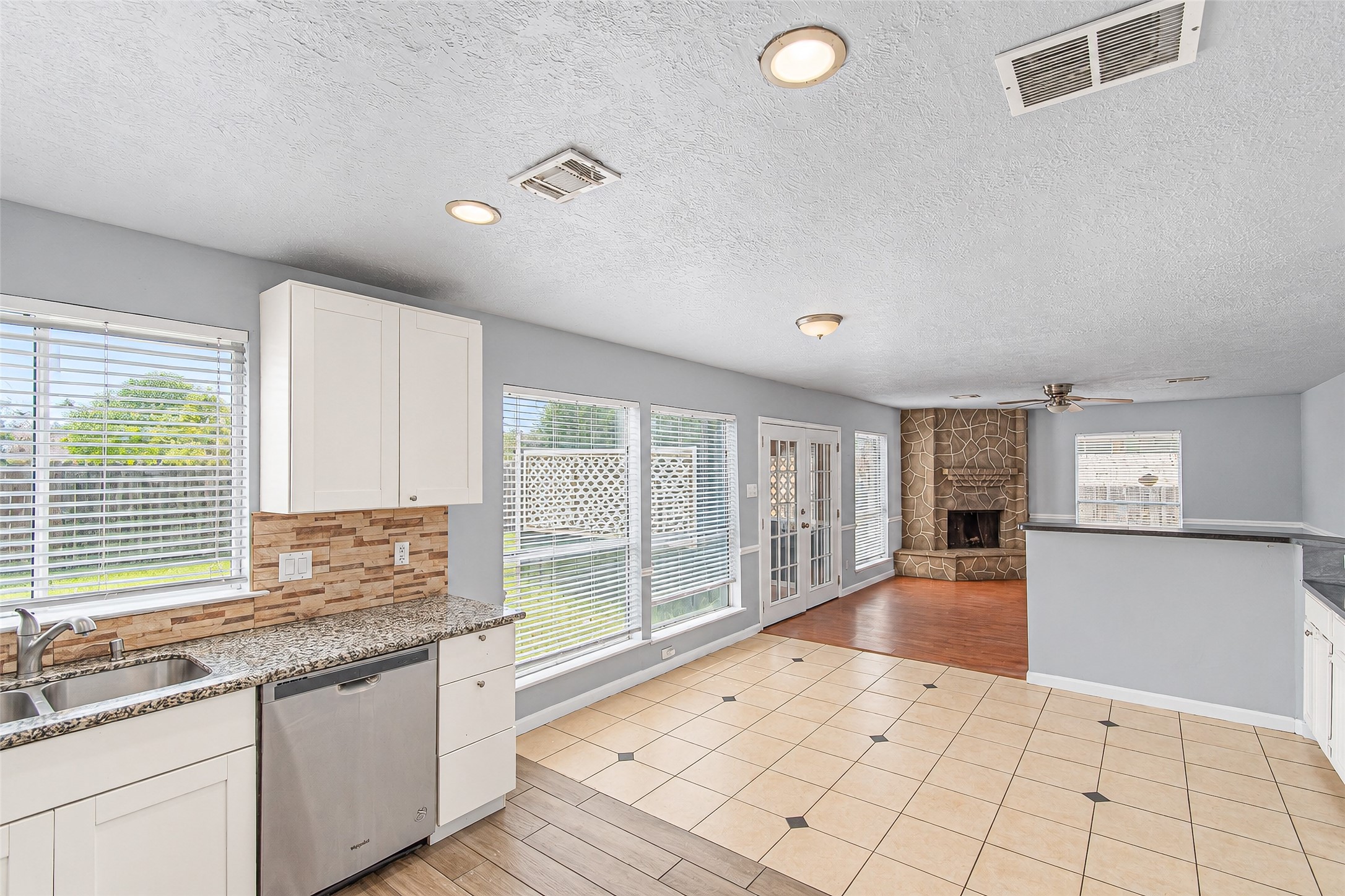 Bright and spacious kitchen and living area featuring large windows, a cozy stone fireplace, modern cabinetry, and an open layout perfect for entertaining.
