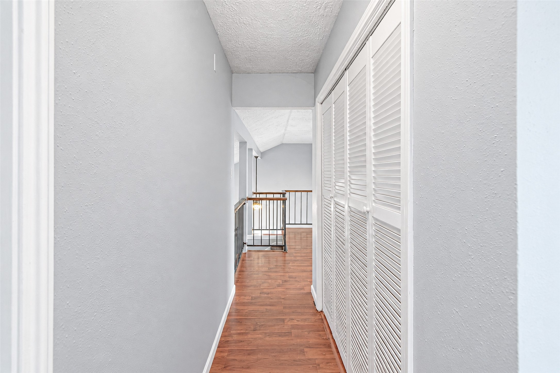 Bright hallway with elegant wood flooring and ample closet space, leading to an airy open railing overlooking the living area.