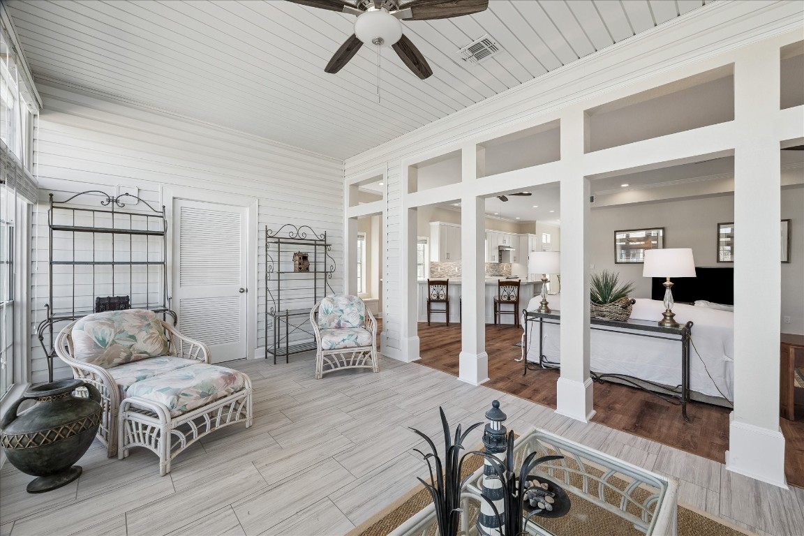 This photo showcases a bright and airy sunroom with wicker furniture and tiled flooring, seamlessly connecting to an open-concept living area with warm wood floors and a modern kitchen. The space is inviting and perfect for relaxation and entertaining.