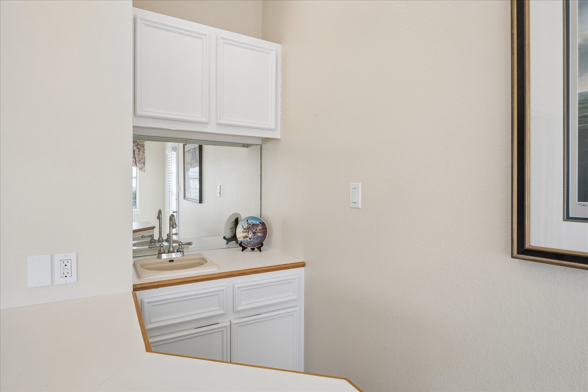 This photo showcases a small wet bar area with white cabinetry, a mirror backsplash, and a sink, ideal for entertaining or adding a touch of luxury to your home.