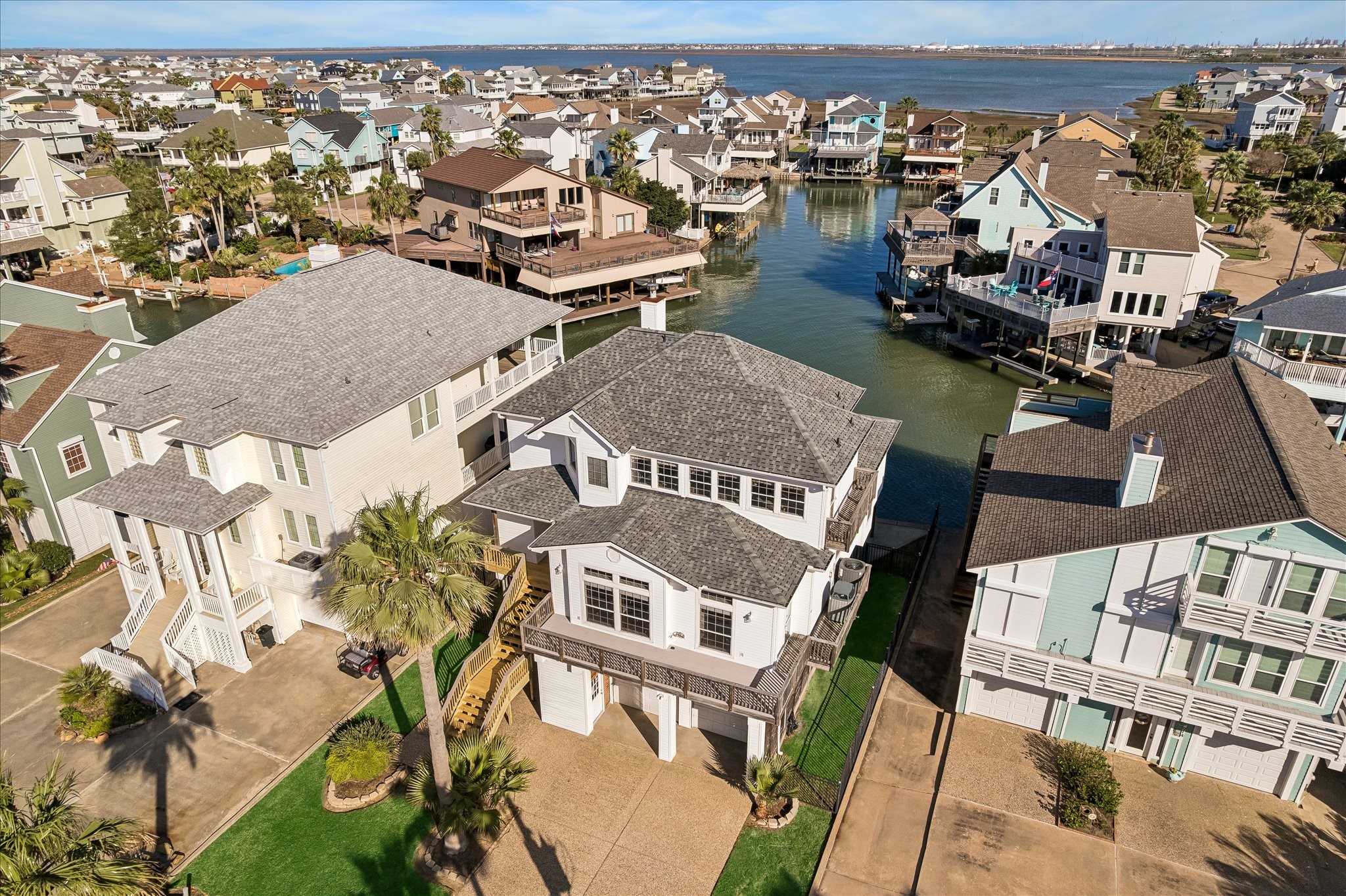 This photo showcases a waterfront home with a modern design, nestled in a picturesque coastal neighborhood. The property features a spacious driveway, direct access to a canal, and is surrounded by well-maintained homes with scenic water views. Ideal for those seeking a serene and scenic living environment.