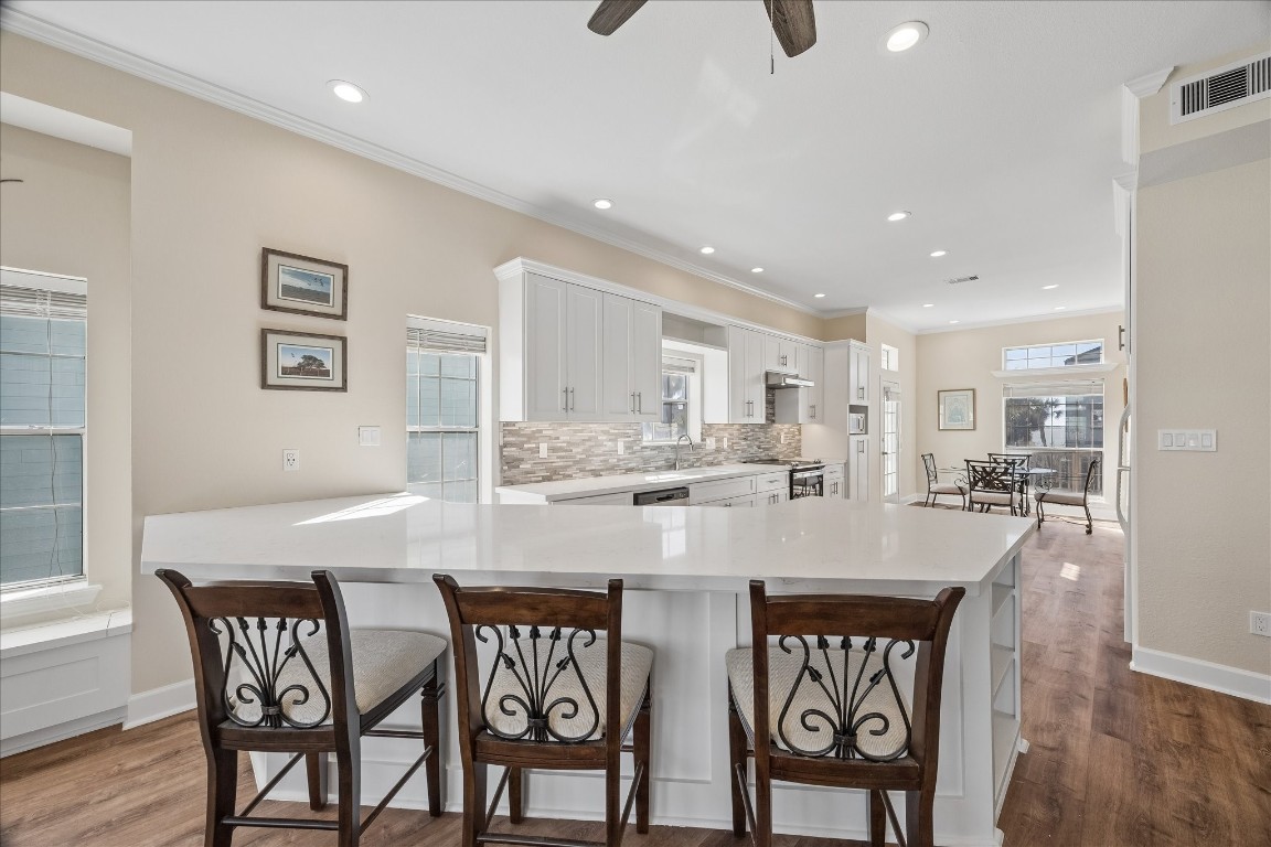 Bright and spacious kitchen with modern white cabinetry, a large island with seating, and hardwood floors. The open layout leads to a dining area, enhanced by ample natural light from multiple windows.