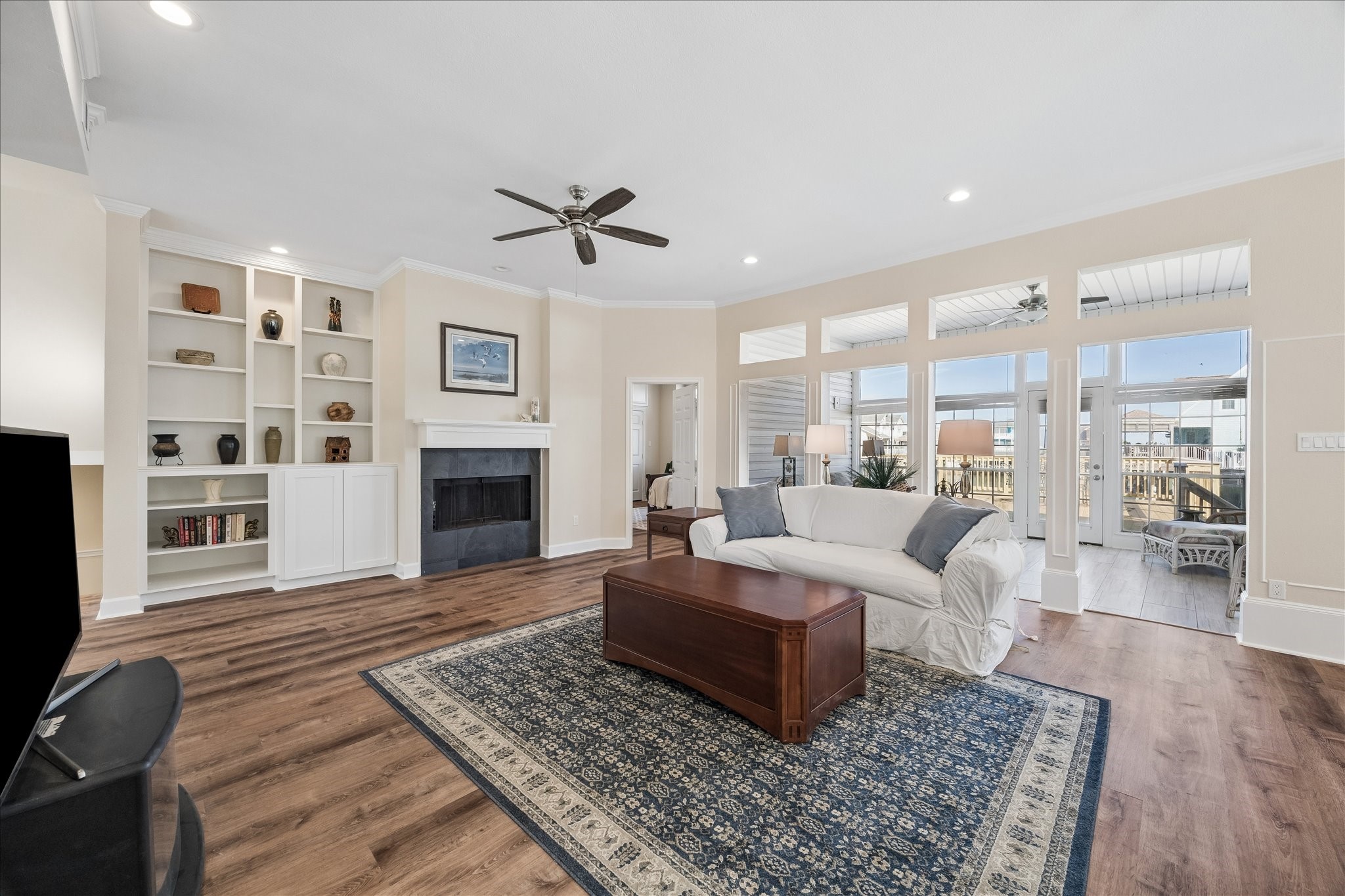 This spacious living room features a cozy fireplace with built-in shelving, large windows allowing plenty of natural light, and stylish wood flooring. A comfortable seating area and neutral tones create an inviting atmosphere, perfect for relaxation and entertaining. This spacious living room features a cozy fireplace with built-in shelving, large windows allowing plenty of natural light, and stylish wood flooring. A comfortable seating area and neutral tones create an inviting atmosphere, perfect for relaxation and entertaining.
